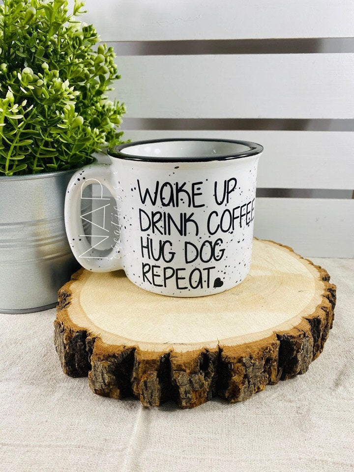 Ceramic campfire mug with the phrase 'Wake Up Drink Coffee Hug Dog Repeat' printed on one side, perfect for dog lovers.