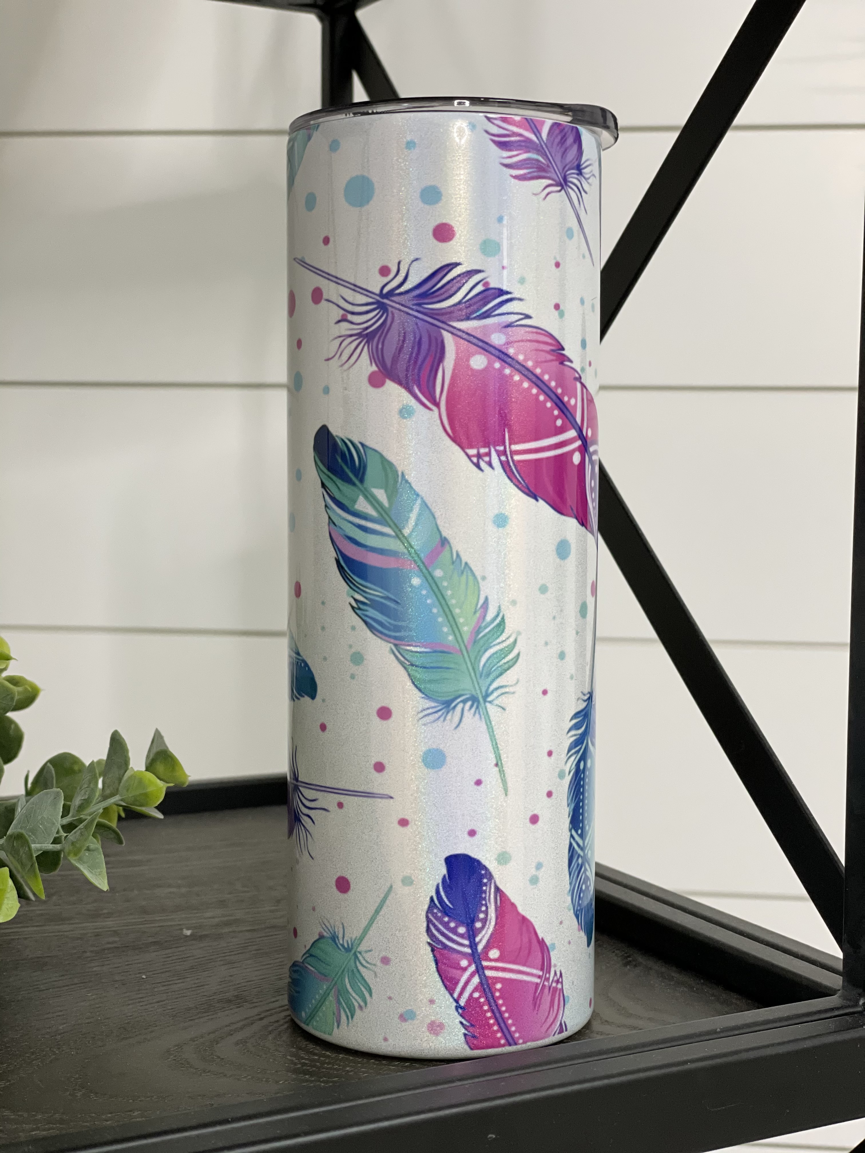 A stylish 20oz skinny tumbler featuring a vibrant watercolor feather design with a shimmering effect, perfect for drinks on the go.