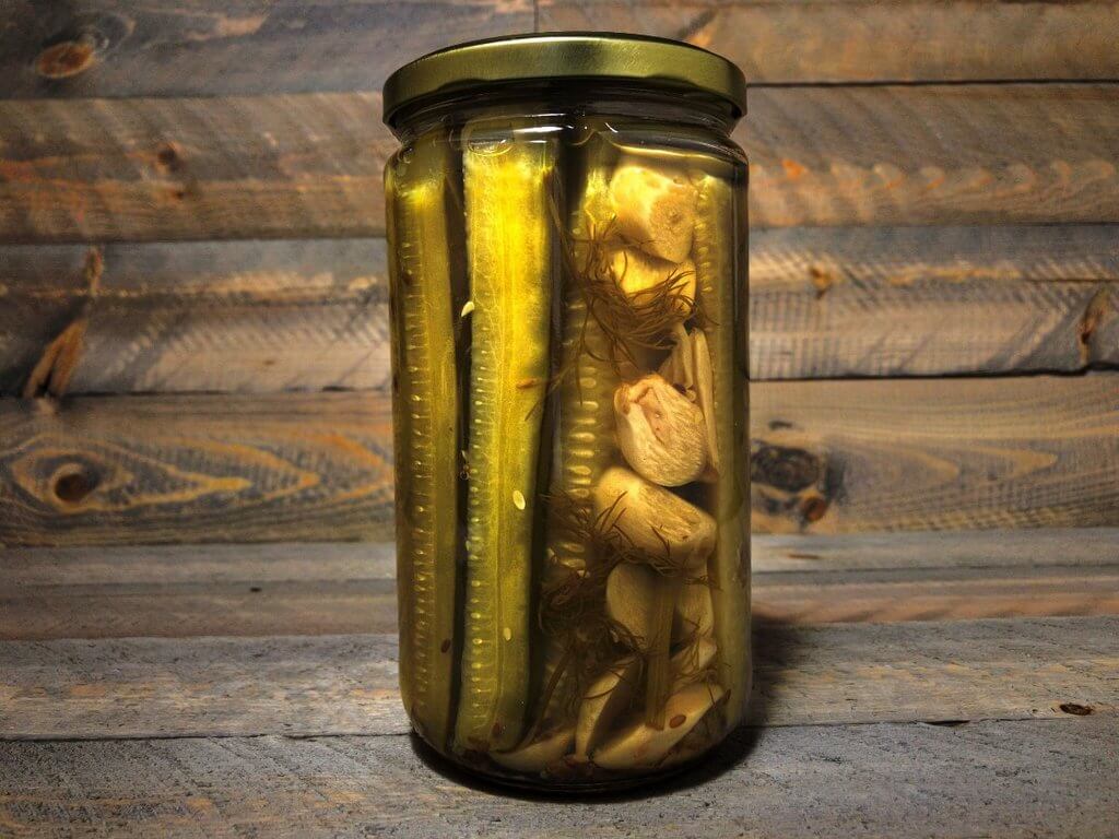 A jar of Aunt Stella's Authentic Polish Garlic Dill Pickle Chips showcasing round slices of pickles with fresh garlic and dill.