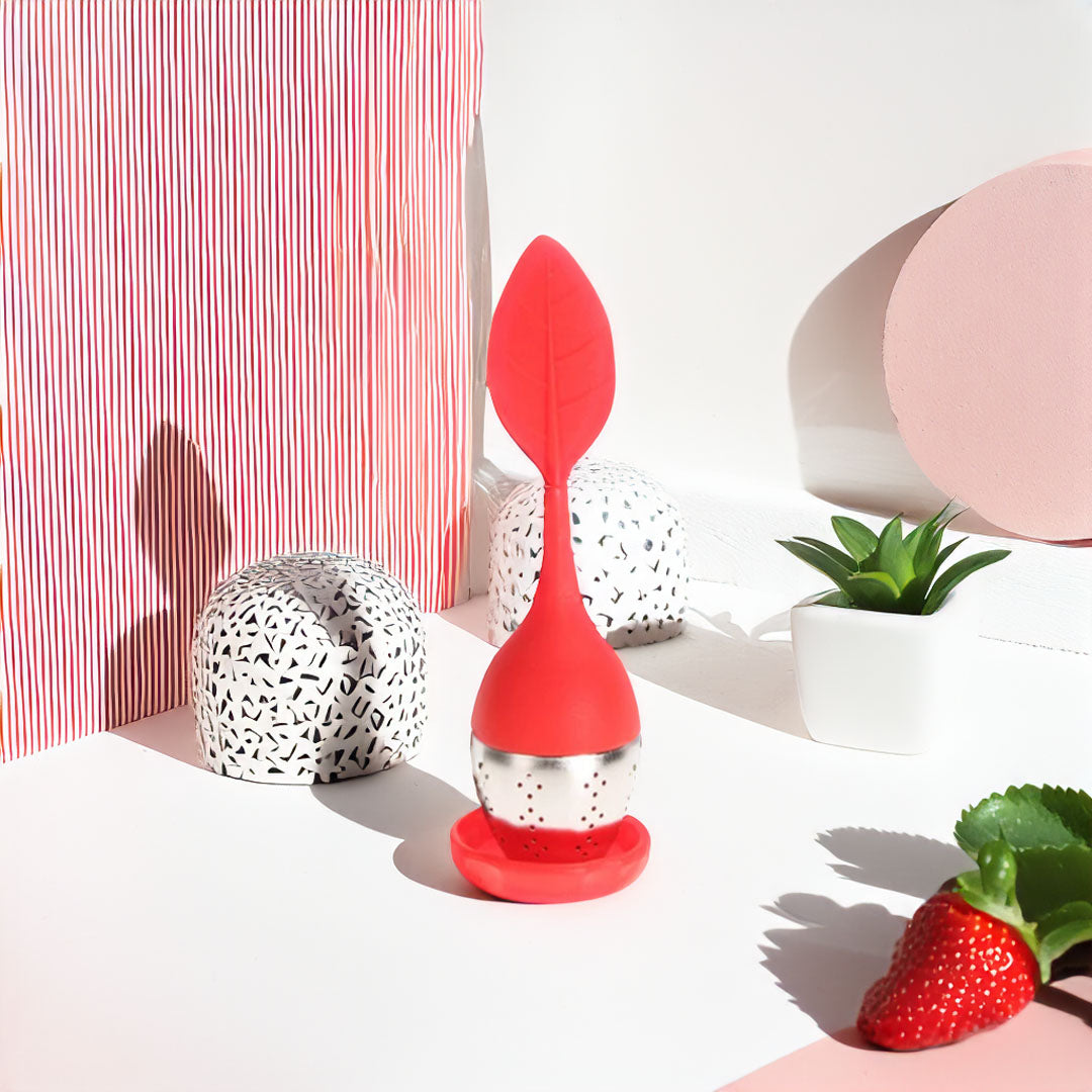 Boule à thé en silicone colorée avec un design moderne, remplie de thé en vrac, posée sur un support.