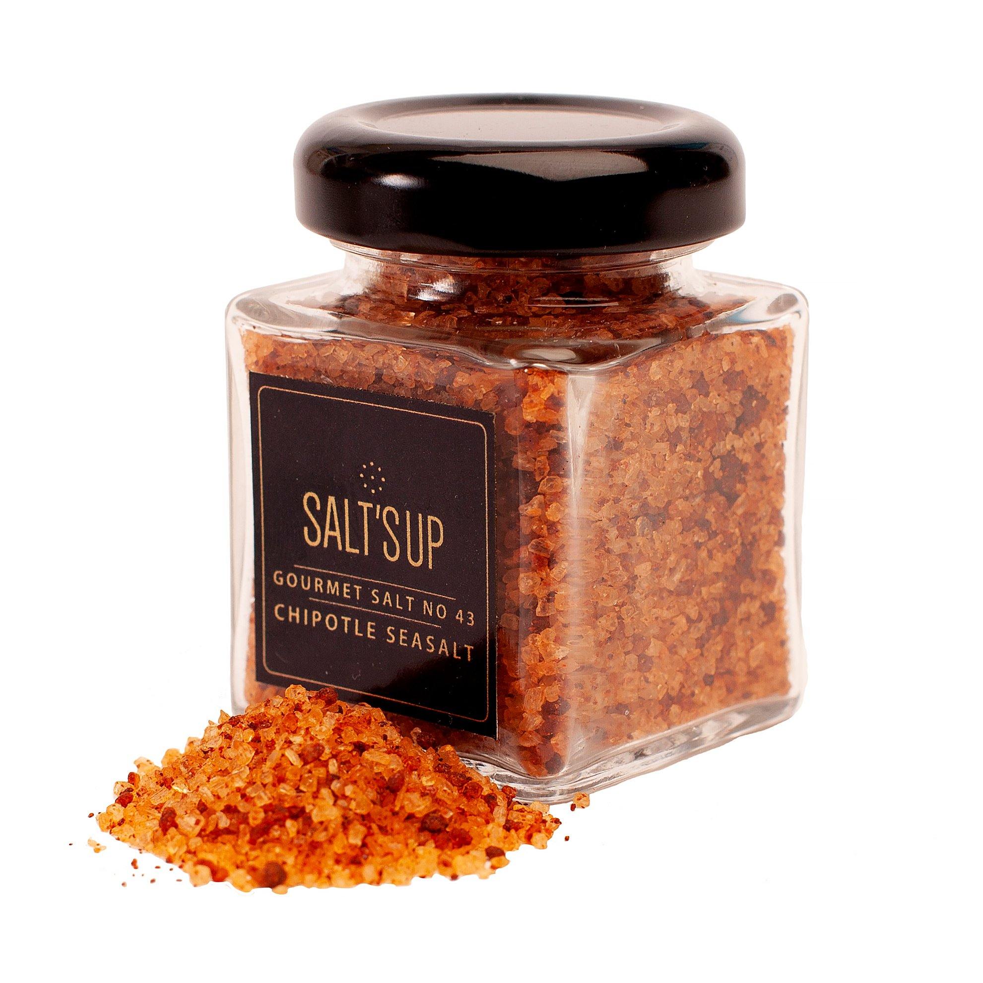 A glass jar of CHIPOTLE gourmet salt showcasing its vibrant orange-red color, surrounded by spices.