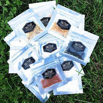 A collection of 19 gourmet salt testers in various colors and textures, showcasing smoked salts, white flakes, and Black Lava salt in elegant packaging.