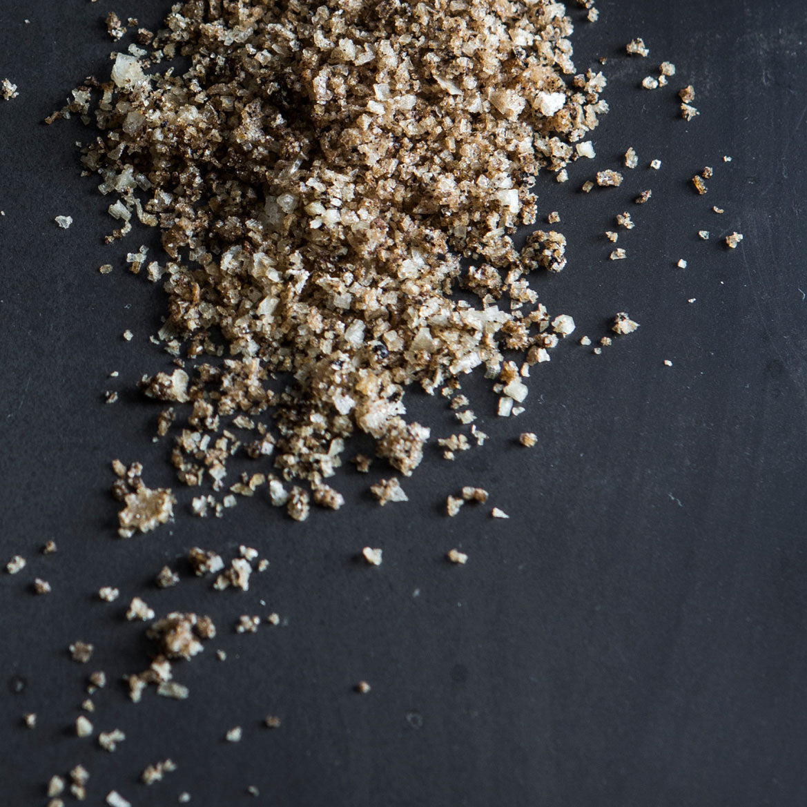 A jar of Licorice Salt showcasing its dark granules mixed with crunchy white flakes, perfect for enhancing sweet and savory dishes.