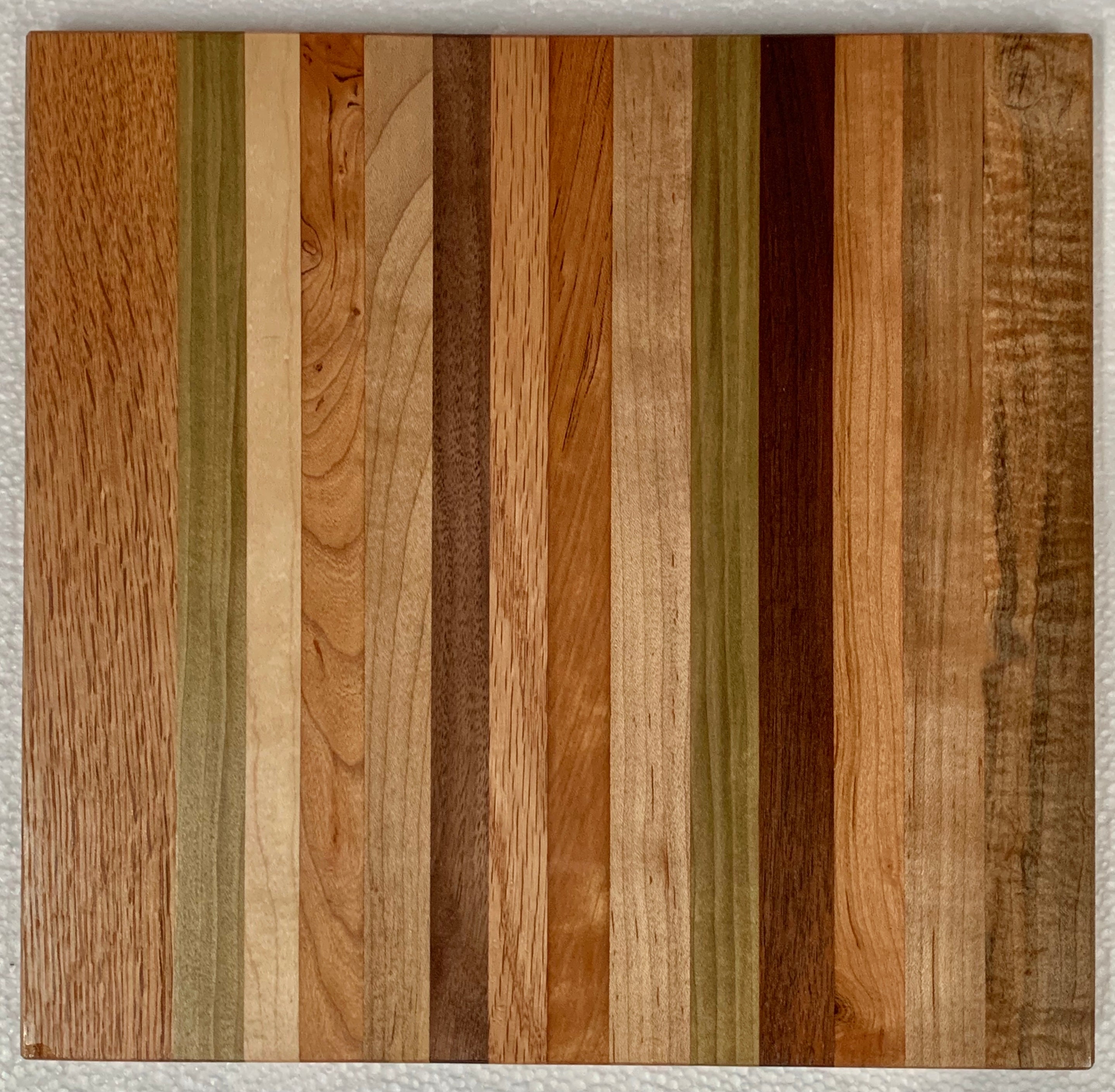 A vibrant multicolored medium wooden cutting board, ideal for serving cheese and snacks, measuring 11 in x 11.5 in.