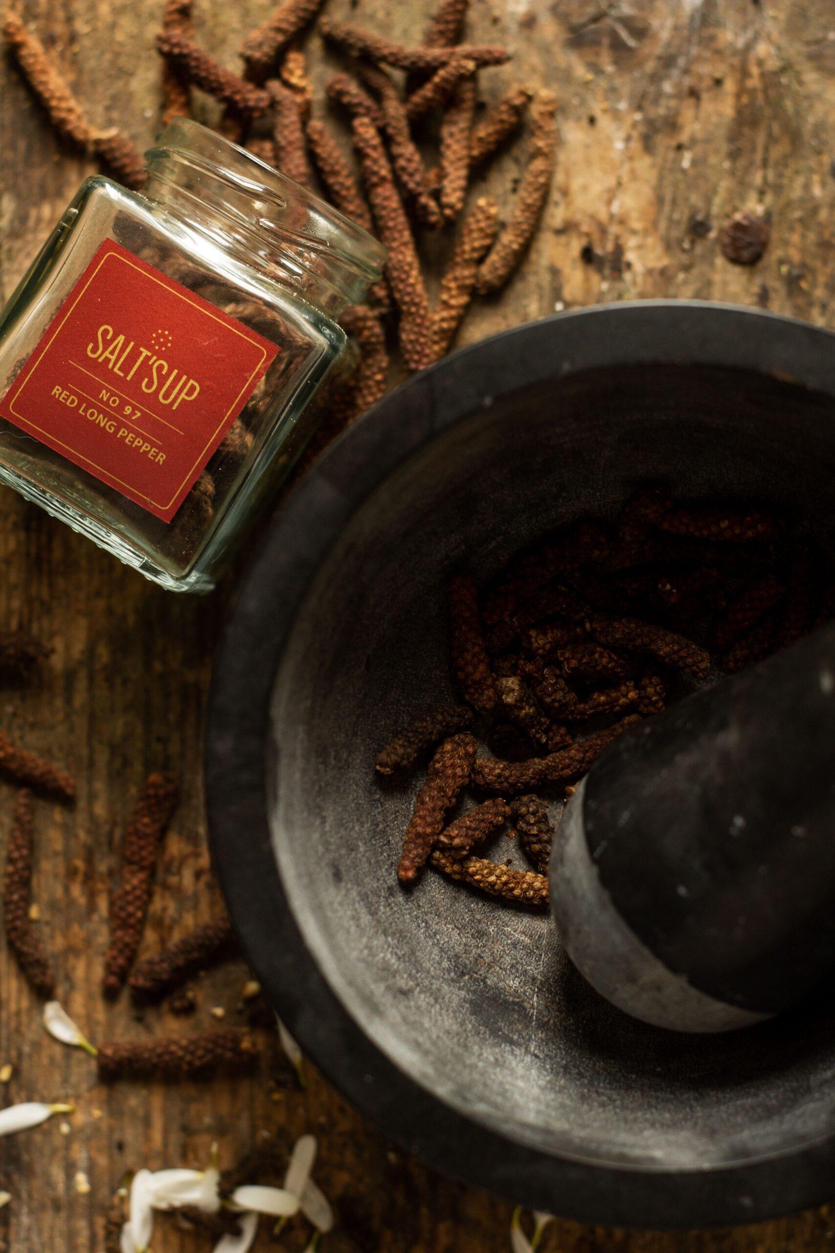 A glass jar filled with vibrant red long pepper, showcasing its unique elongated shape and rich color, perfect for culinary use.