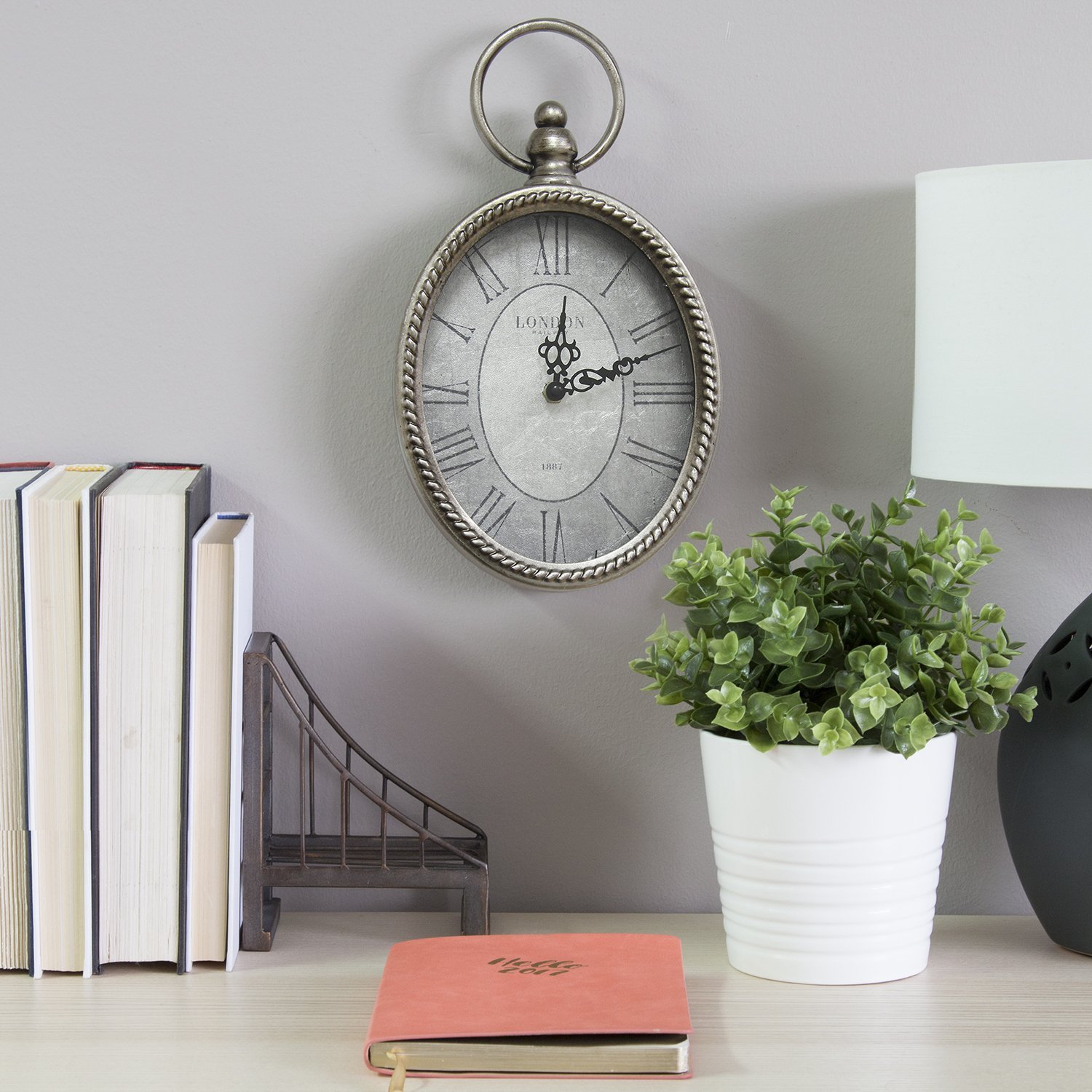 11.75-inch oval vintage wall clock with Roman numerals and antique silver background, showcasing a stylish metal and glass design.