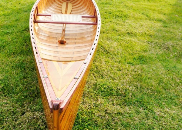 Handcrafted wooden canoe with ribs and curved bow, showcasing clear graded cedar and fiberglass epoxy finish.