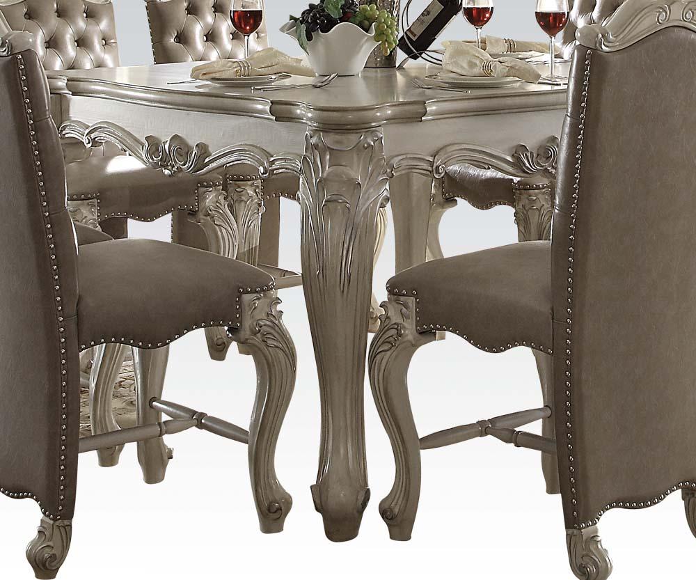 Bone White Wooden Top dining table with decorative base and oversized scrolled feet, complemented by upholstered chairs with button tufting.