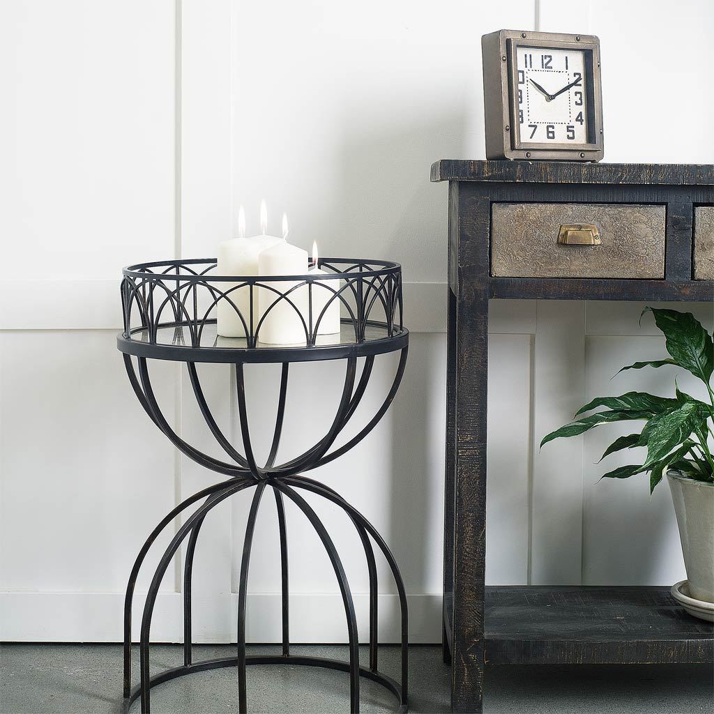 Hour-glass shaped accent table with a mirrored top and black iron base, showcasing a modern and elegant design.