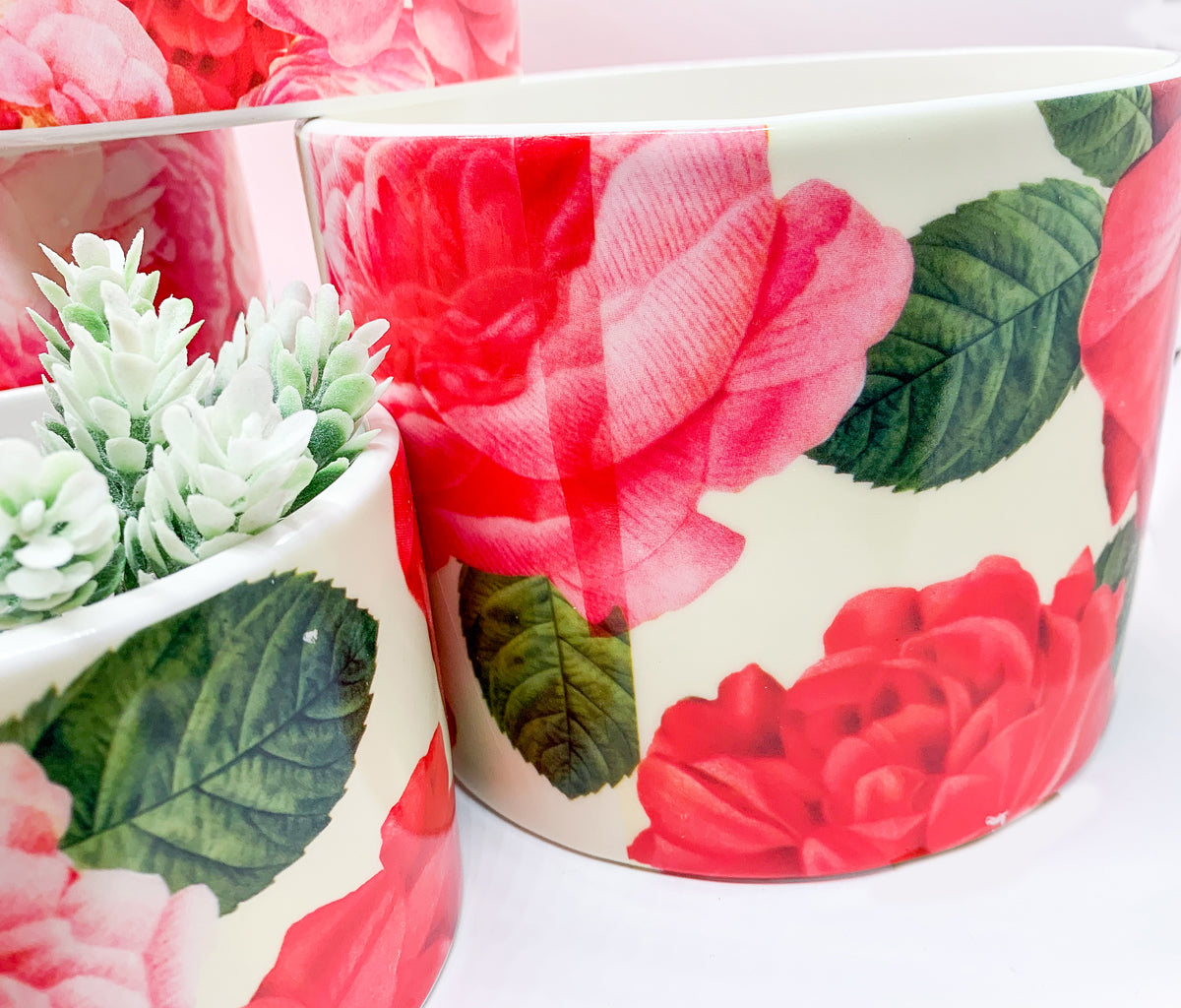 Two stunning Rose Marie floral cachepots in pink and red ceramic, showcasing intricate rose patterns.