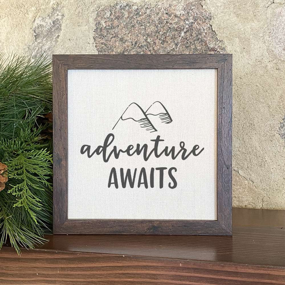 Adventure Awaits framed sign with a wood frame and linen-look background, showcasing a mountain theme.