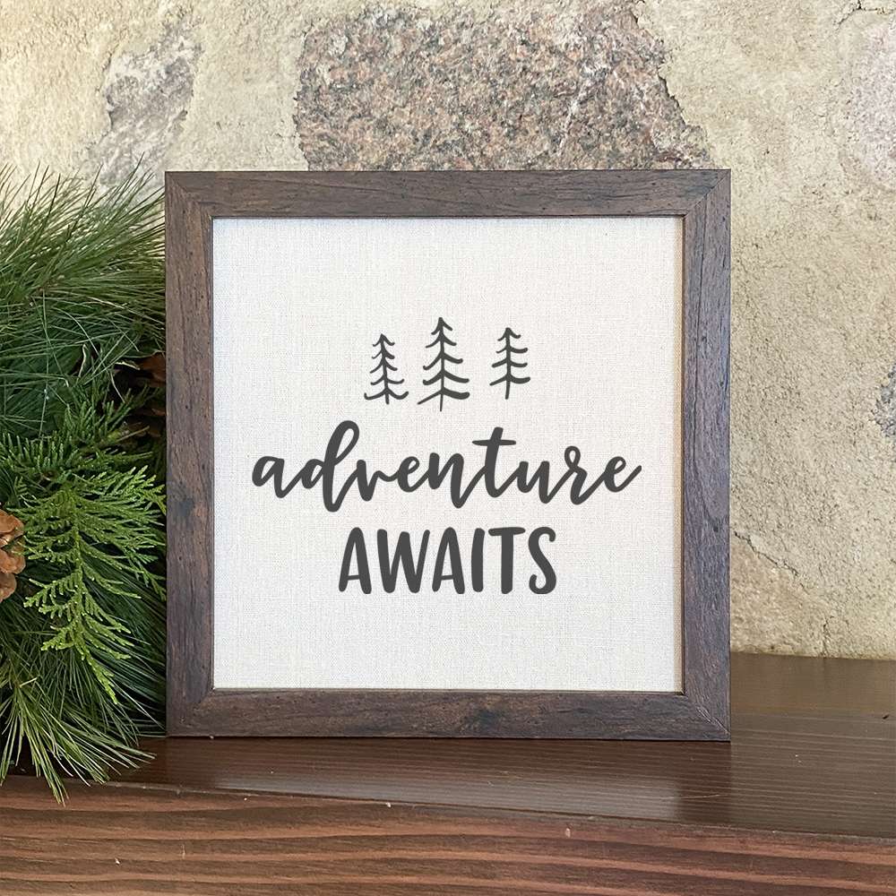 Adventure Awaits framed sign with a wood frame and linen-look background, featuring nature-inspired design.
