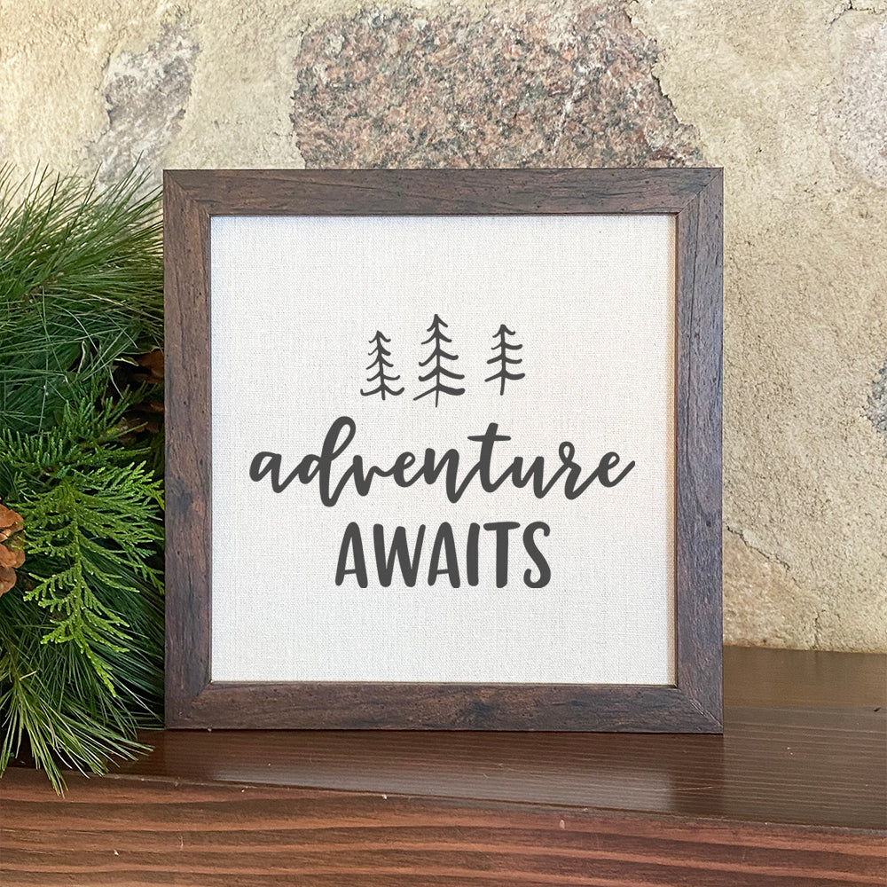 Adventure Awaits framed sign with a wood frame and linen-look background, featuring nature-inspired design.