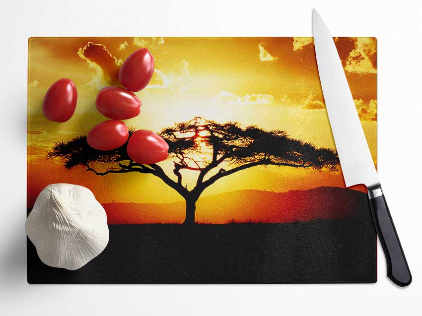 A beautiful chopping board featuring an African tree silhouette against a vibrant sunset, made from durable tempered glass.