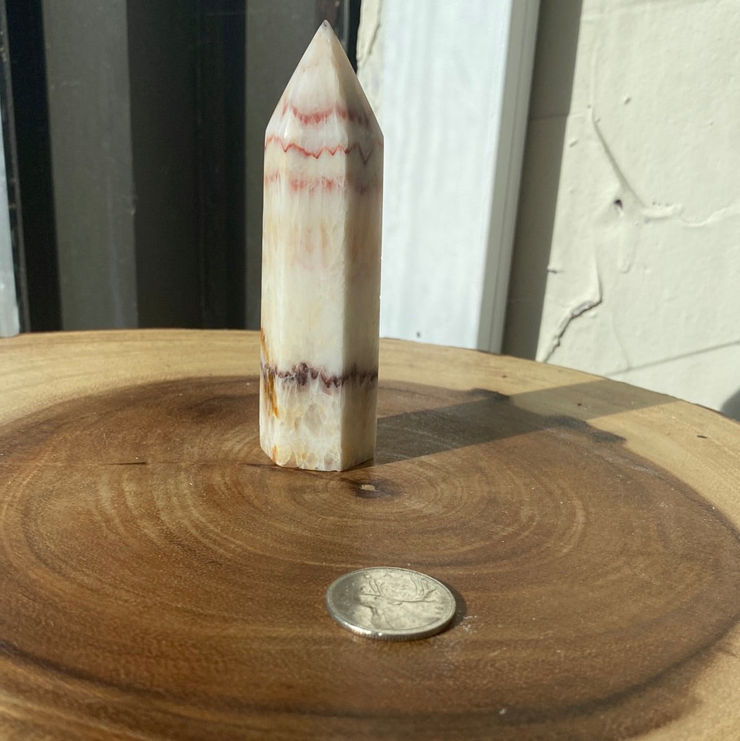 A polished Banded Calcite Point showcasing vibrant pink, white, and red stripes, symbolizing peace and harmony.