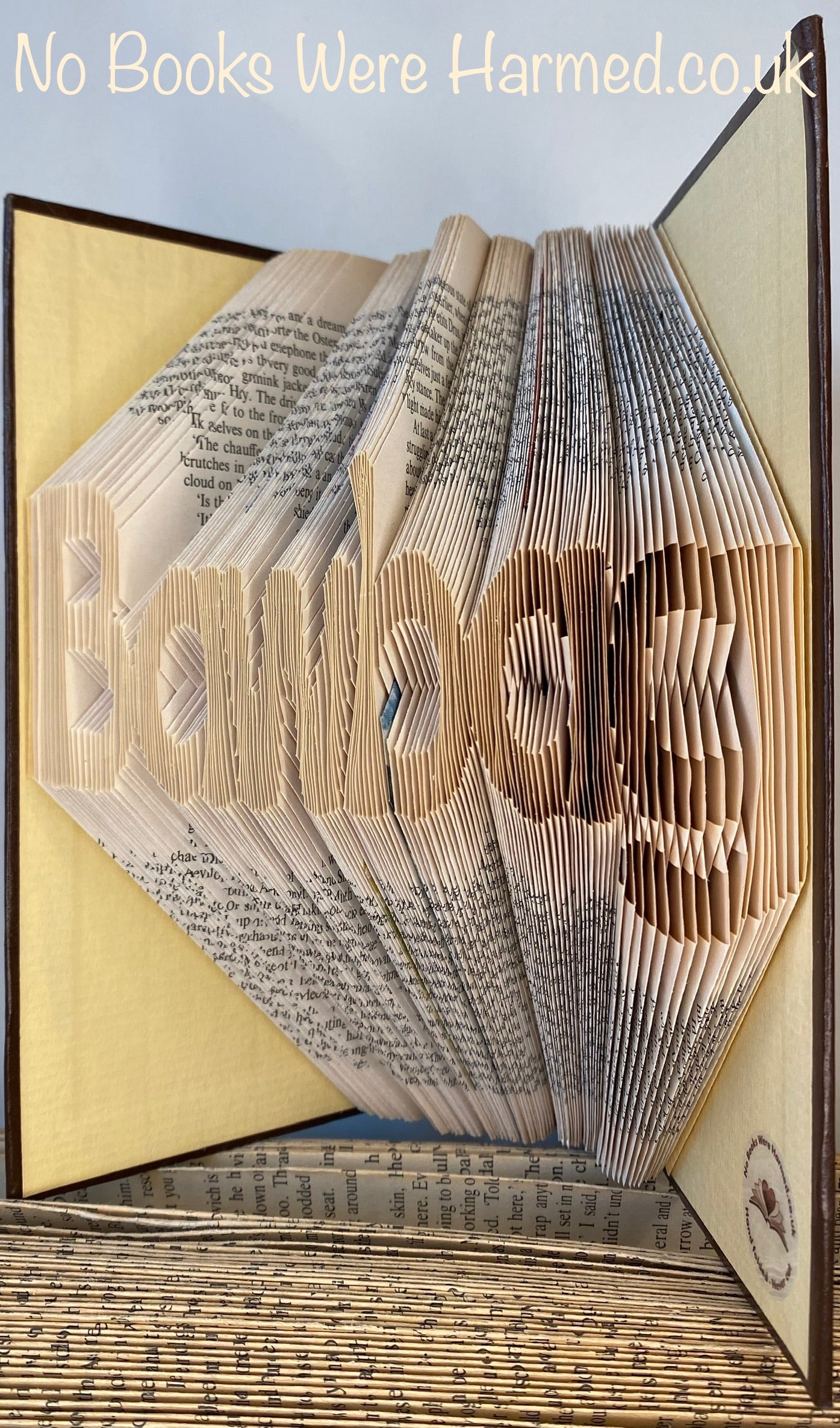 A unique hand-folded book art piece shaped like a bawbag, crafted from vintage book pages, showcasing intricate folds and a playful design.