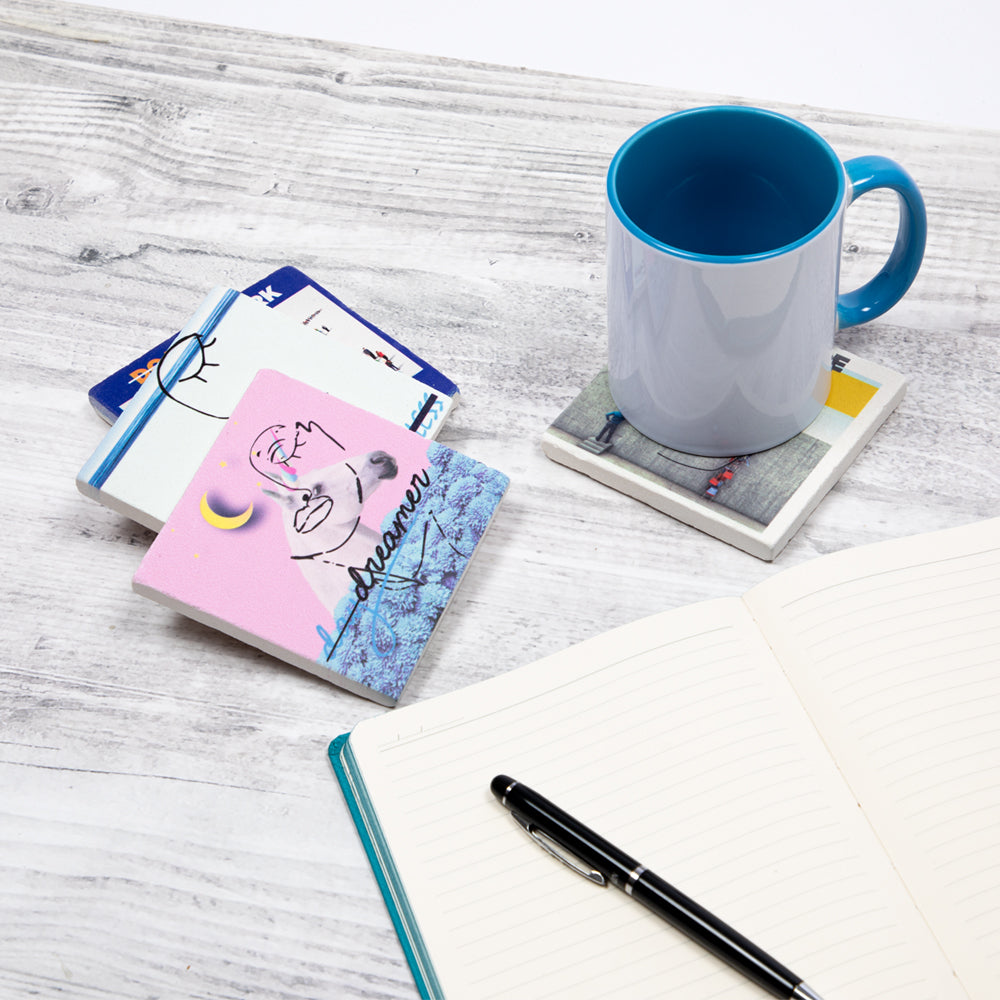 Set von vier Biggdesign Faces Natursteinuntersetzern aus Kalkstein mit bunten Designs und Korkbasis.