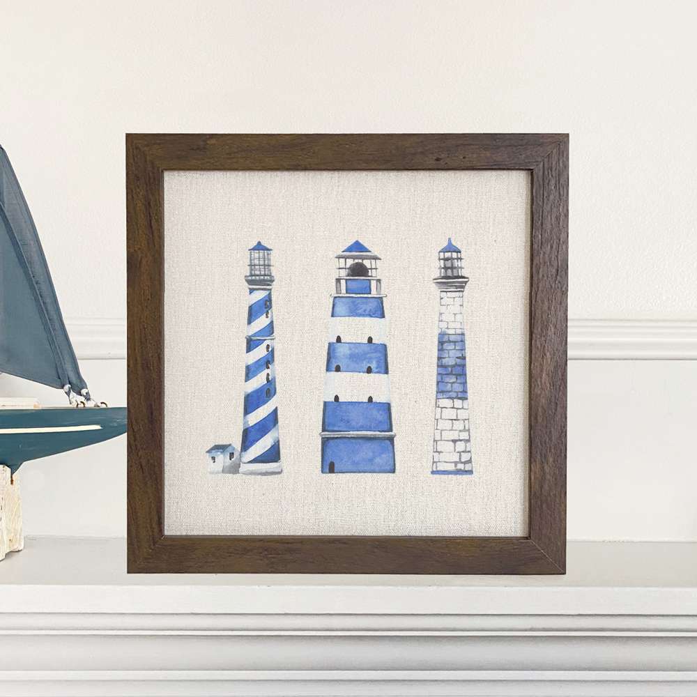 A beautifully framed sign featuring blue lighthouses on a neutral linen-look background, perfect for home decor.
