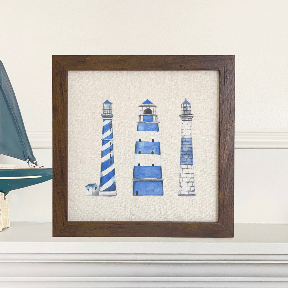 A beautifully framed sign featuring blue lighthouses on a neutral linen-look background, perfect for home decor.