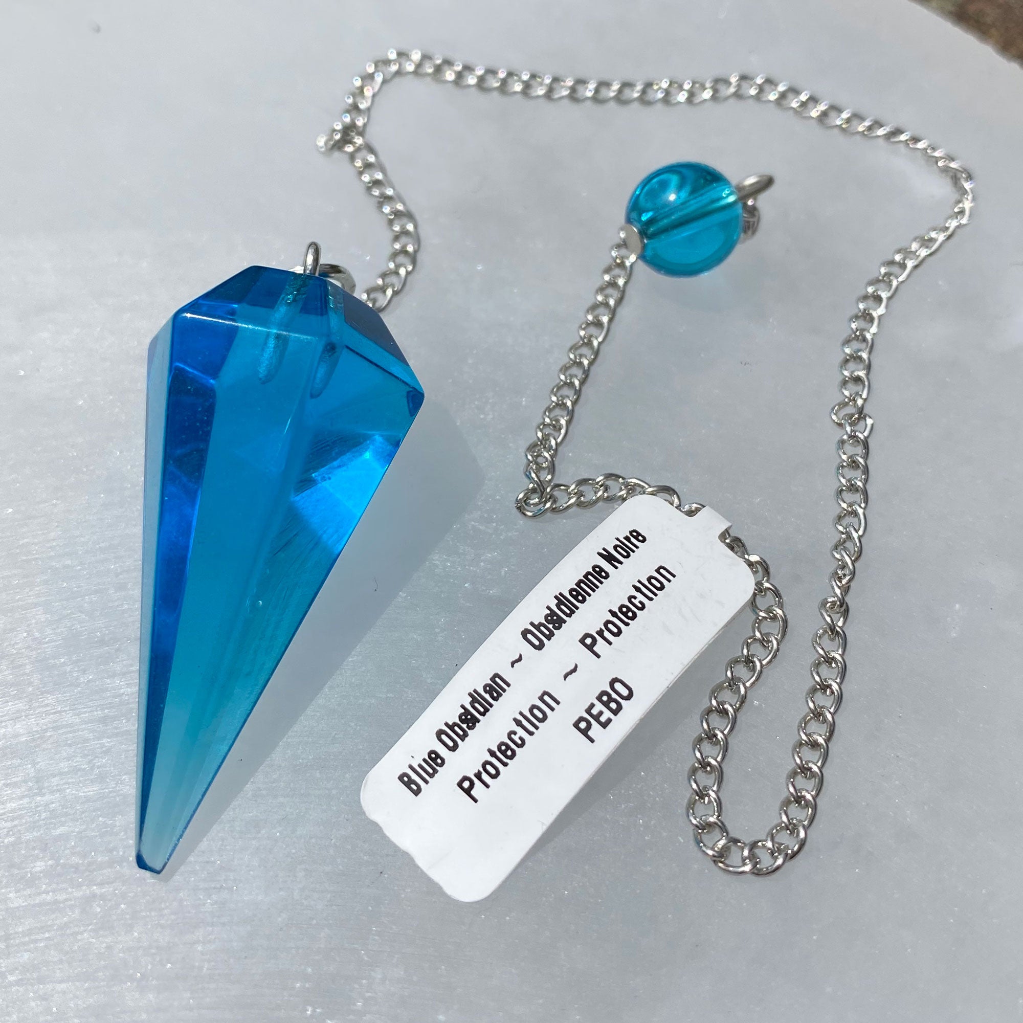 A beautiful Blue Obsidian Pendulum on a silver chain, showcasing its unique color and texture.