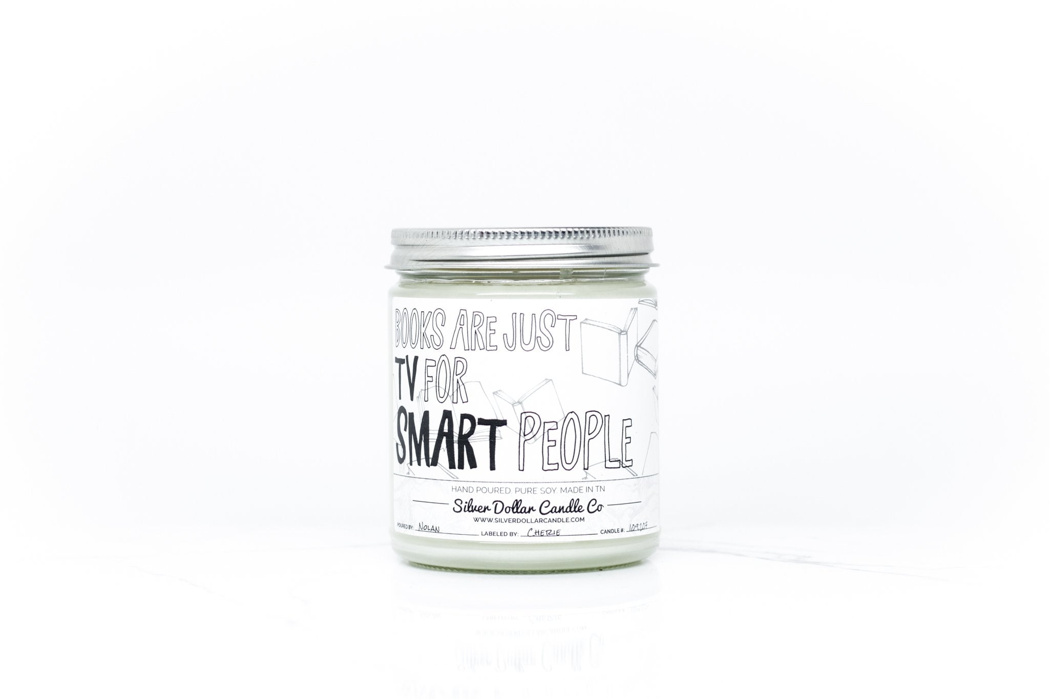 A beautifully designed candle with the phrase 'Books Are Just TV For Smart People', showcasing its elegant packaging and vibrant colors.