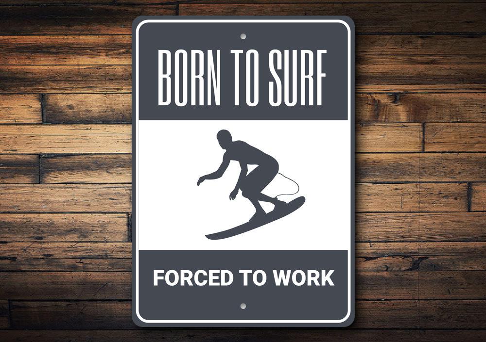 A decorative metal sign reading 'Born to Surf Forced to Work', featuring vibrant colors and a beach-themed design, perfect for coastal decor.