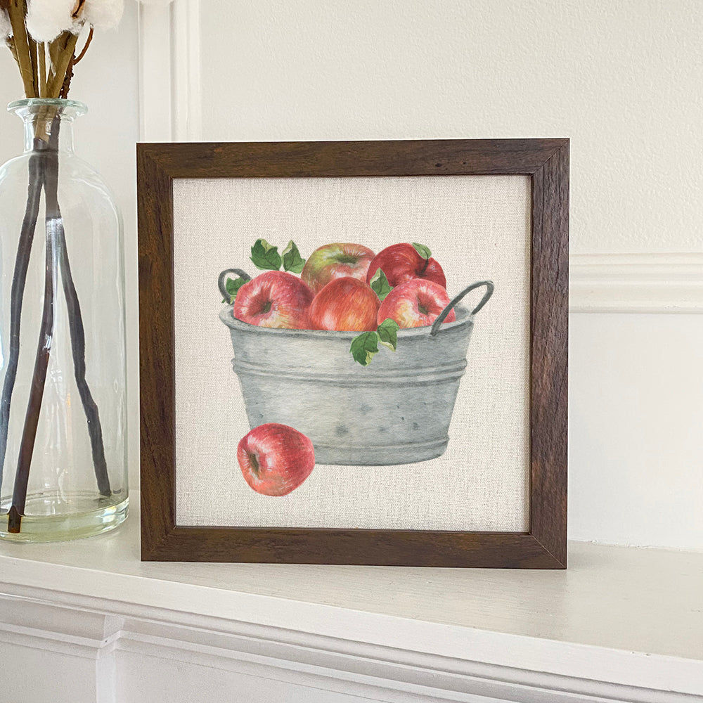 A beautifully framed sign featuring a bucket of red apples, designed with eco-friendly inks on a linen-look background.
