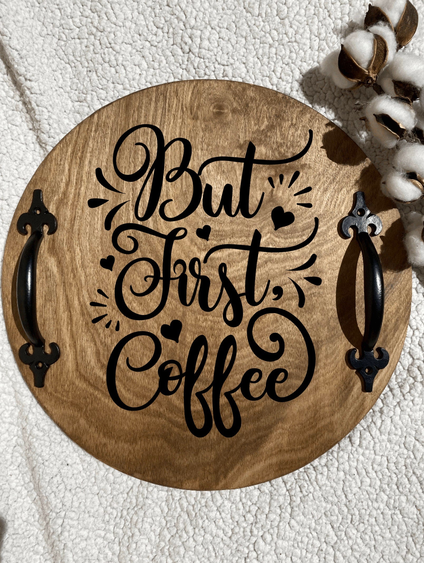 A rustic wooden serving tray with 'But First Coffee' burned into the surface, featuring black metal handles and a rich chestnut stain.