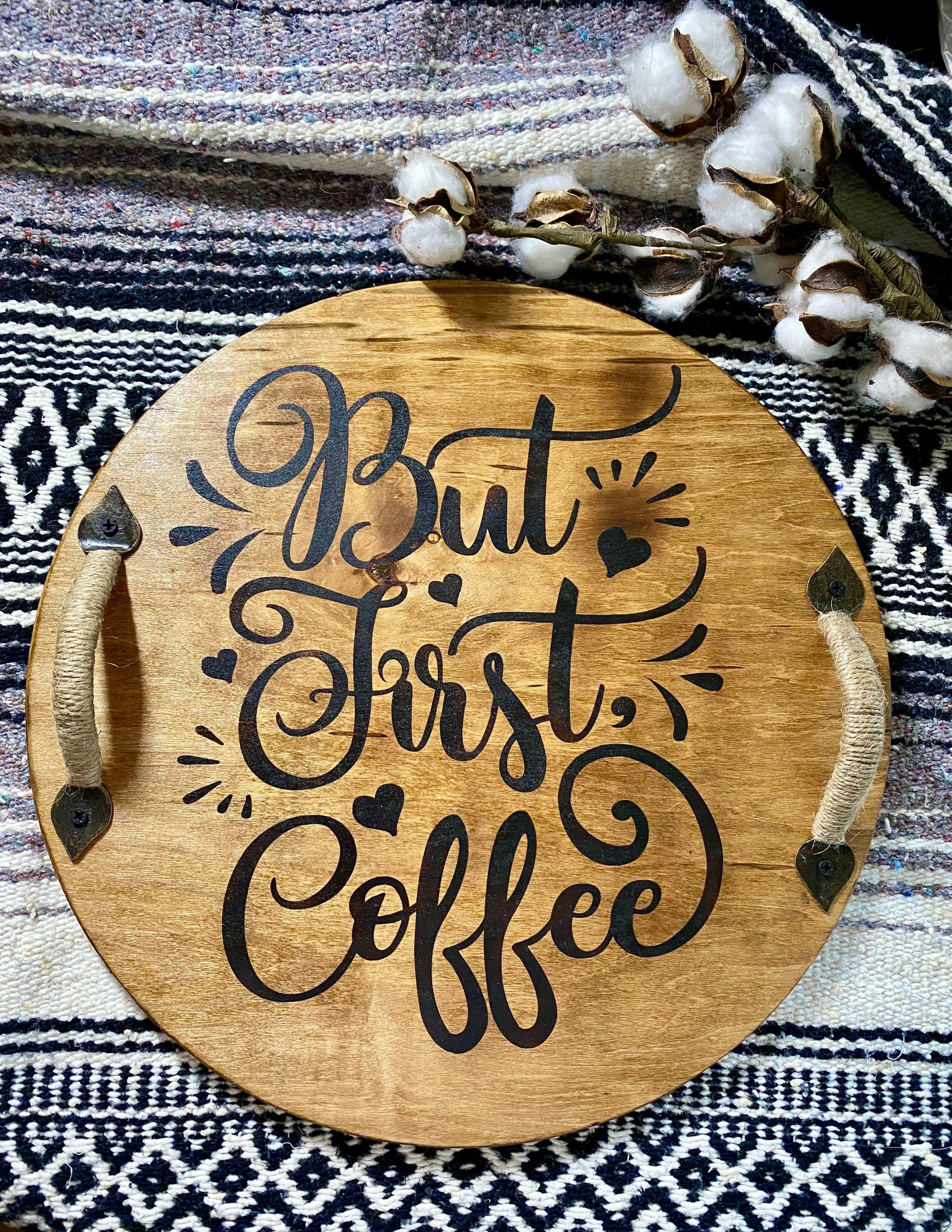 A rustic wooden serving tray with 'But First Coffee' burned into the surface, featuring black metal handles and a rich chestnut stain.