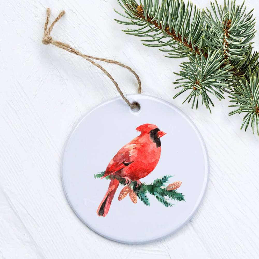 A beautiful Cardinal perched on an evergreen branch, featured on a high-quality porcelain ornament with a glossy finish.