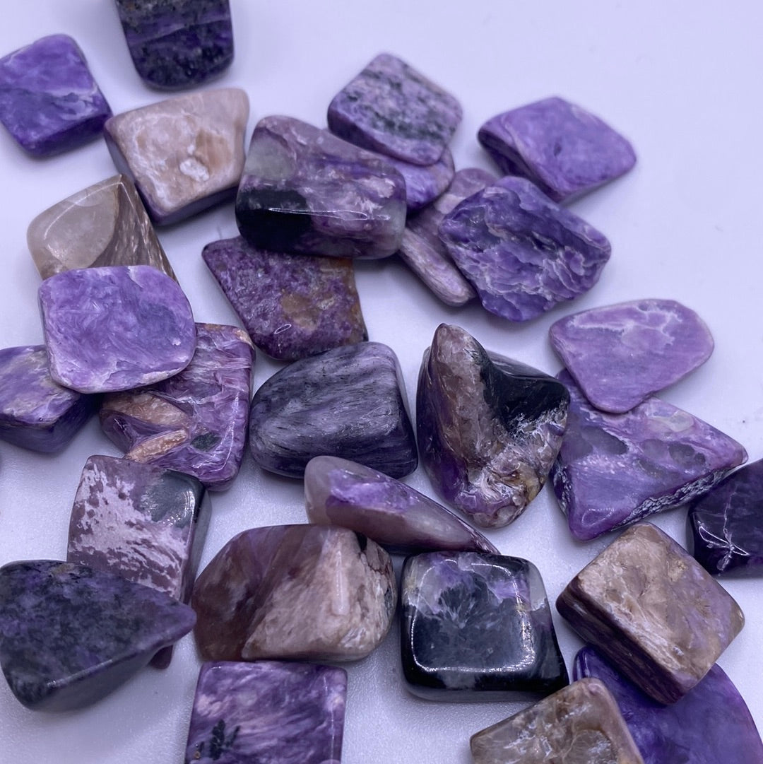 Small tumbled Charoite crystal showcasing purple, grey, and black swirls, symbolizing calmness and protection.