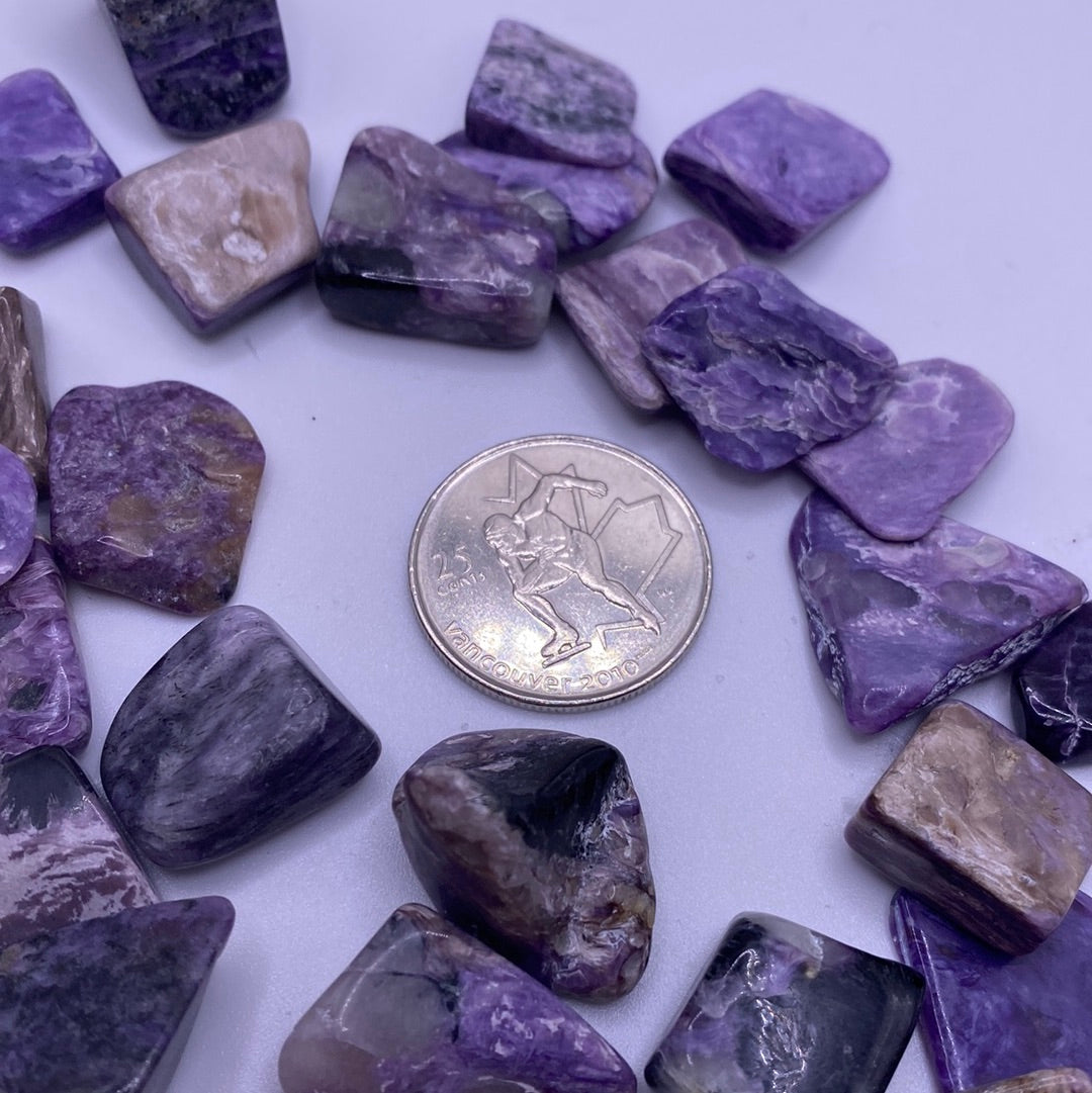Small tumbled Charoite crystal showcasing purple, grey, and black swirls, symbolizing calmness and protection.
