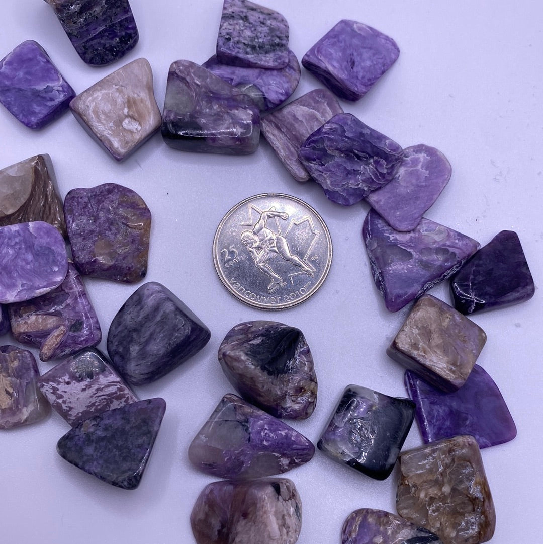 Small tumbled Charoite crystal showcasing purple, grey, and black swirls, symbolizing calmness and protection.