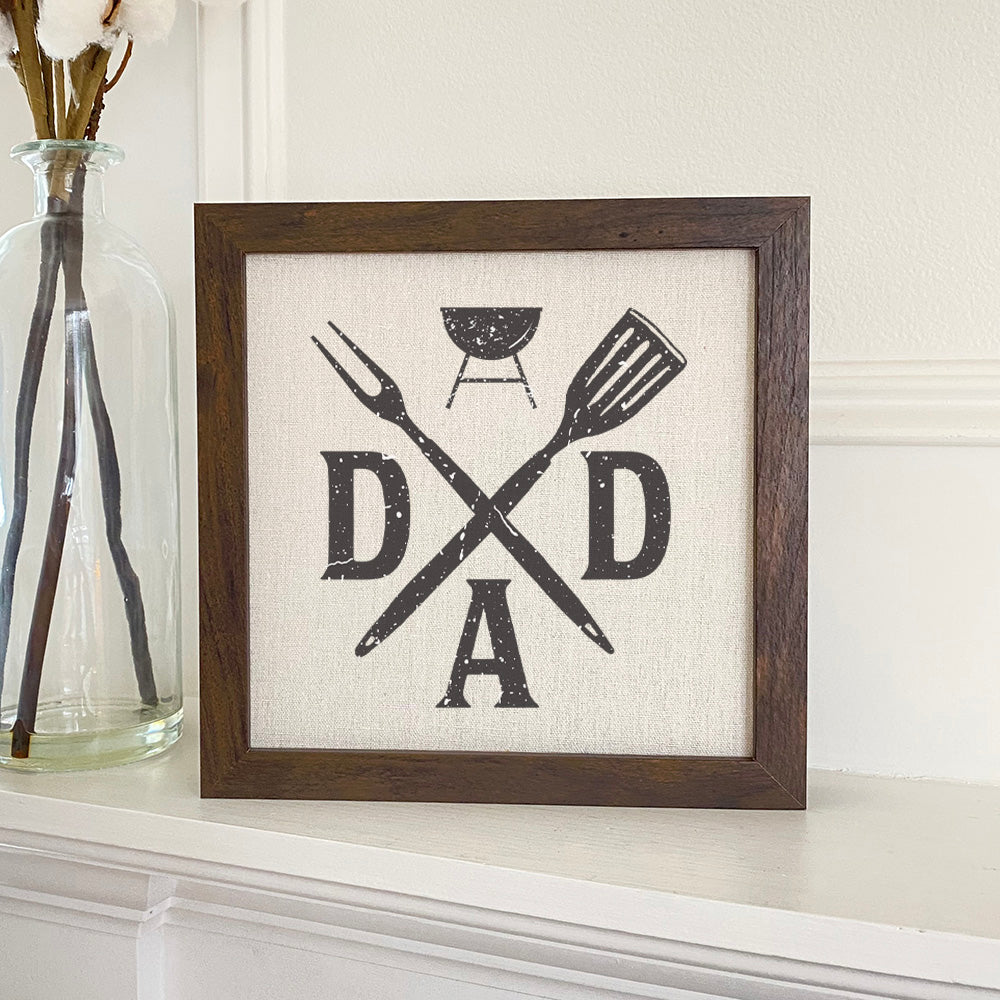 A framed sign featuring a spatula and fork design, set in a stylish wood frame, available in walnut or white-washed finish.