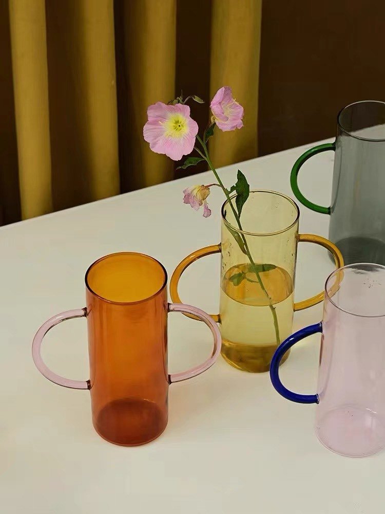 A whimsical dual-handle glass flower vase, handblown with a unique design, perfect for seasonal flowers and elegant table settings.