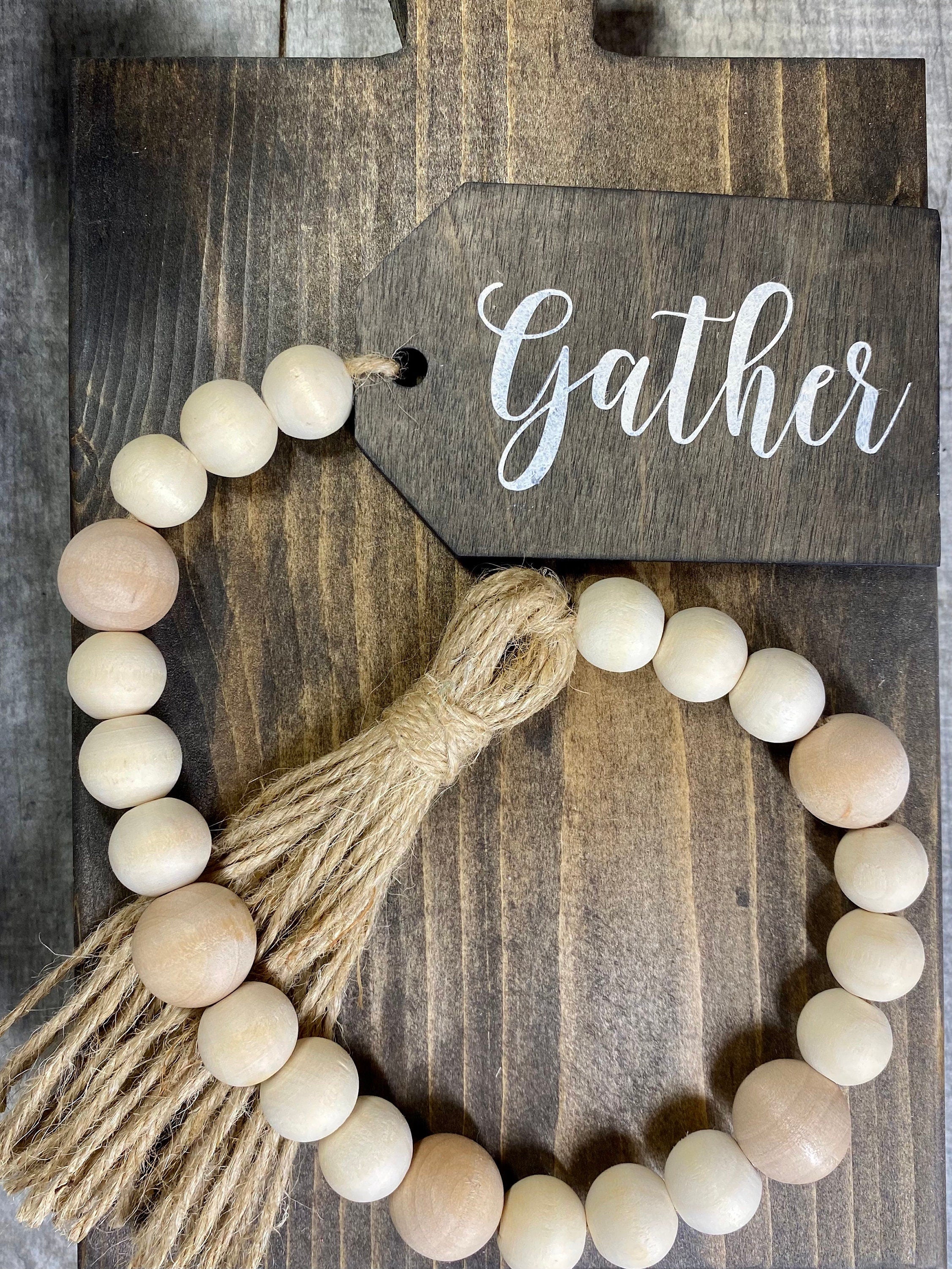 A beautiful Fall wood bead garland featuring natural wooden beads, a jute tassel, and a hand-painted 'Gather' tag, perfect for seasonal decor.