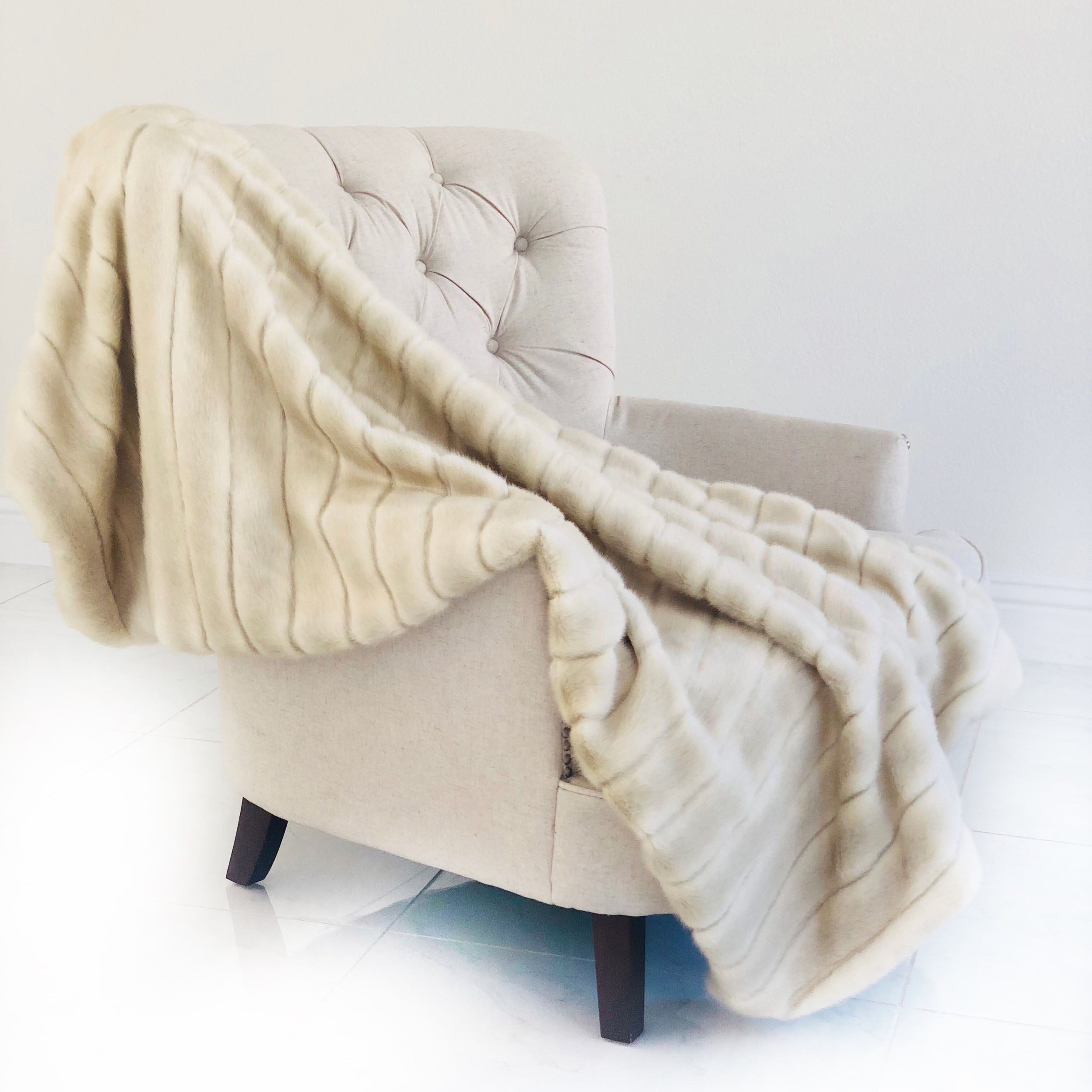 Fancy Mink Faux Fur Ivory Luxury Throw blanket draped elegantly on a couch, showcasing its plush texture and elegant ivory color.