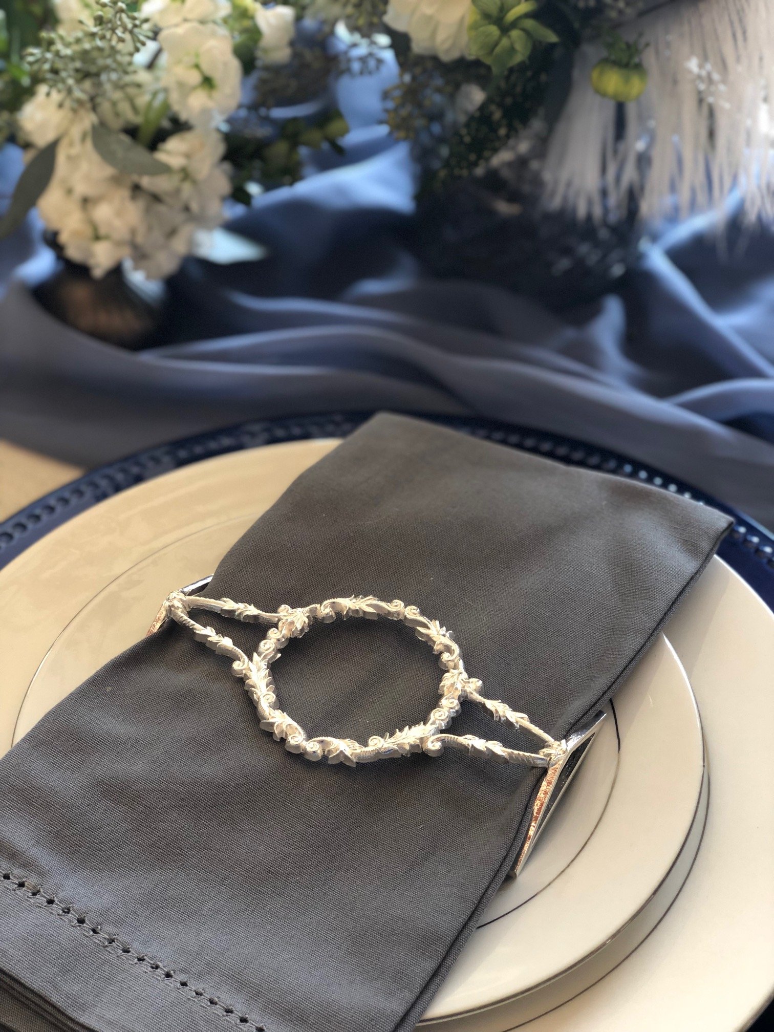 A set of four shiny silver filigree napkin wraps elegantly displayed in a stylish box, showcasing intricate designs.