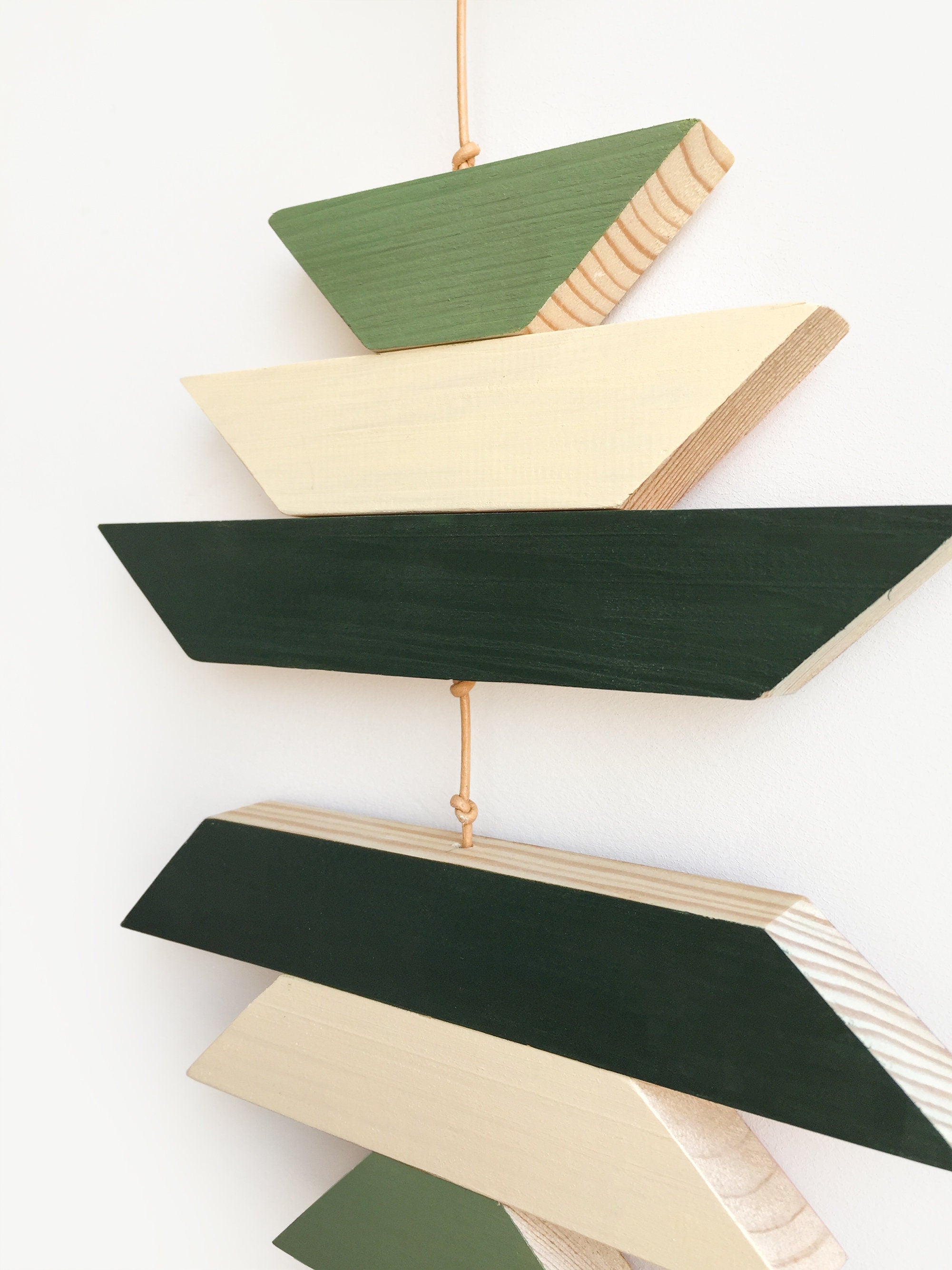 A beautiful geometric green wood wall hanging featuring sage green tones, connected with light brown cotton cord, perfect for boho decor.