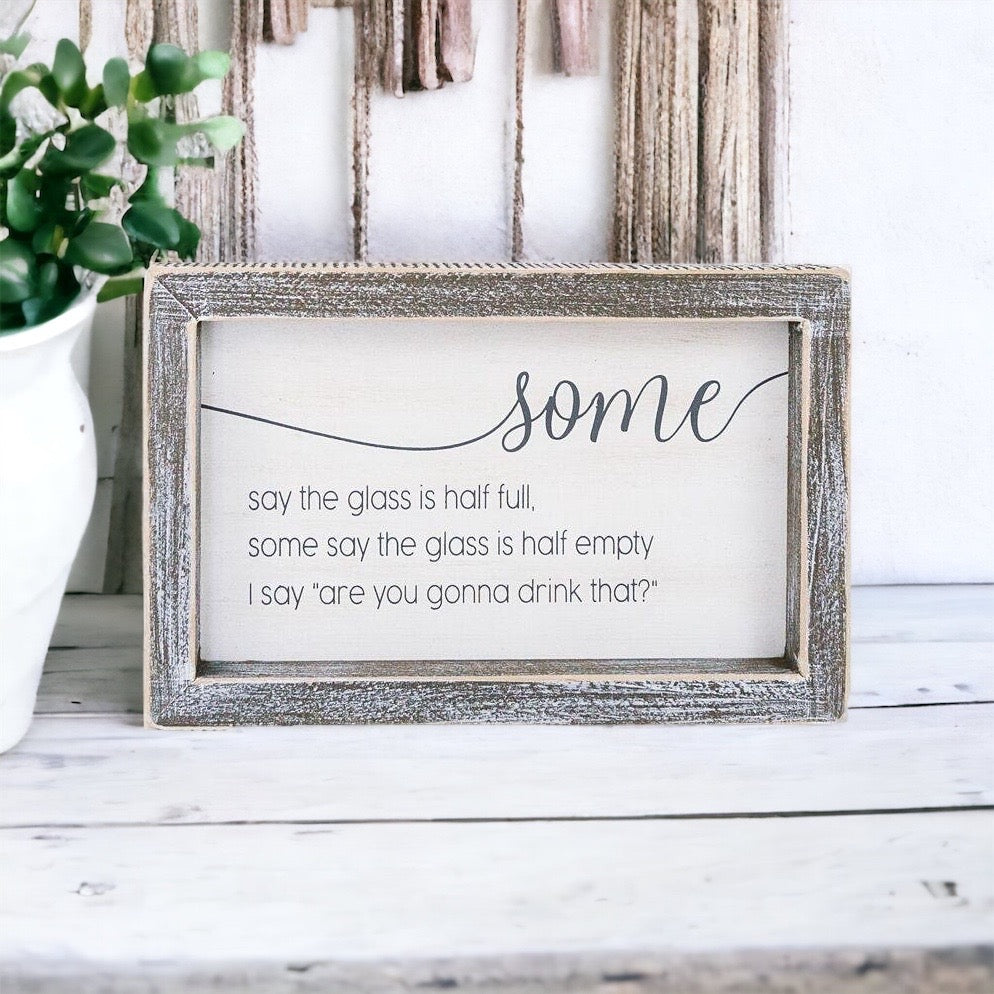 A wooden sign with the phrase 'Half Full or Empty' in white and grey colors, measuring 8 inches wide and 5 inches high.