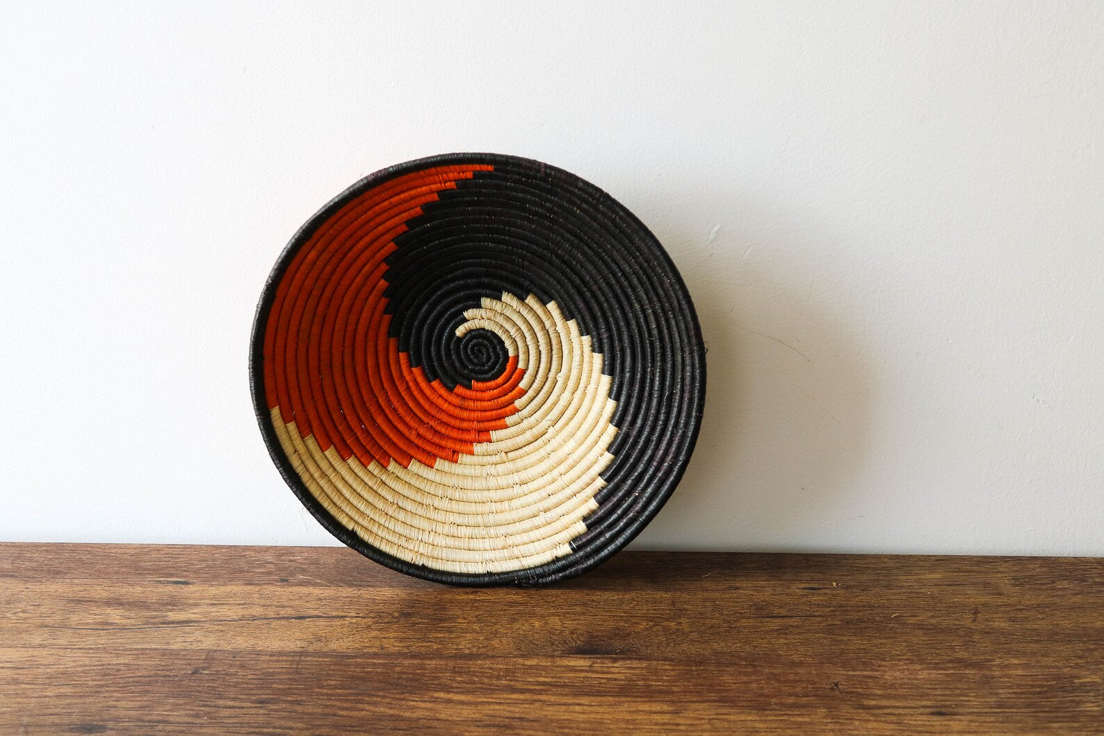 Handwoven African wall hanging basket from Rwanda, showcasing intricate designs and vibrant colors, made from natural raffia grass.