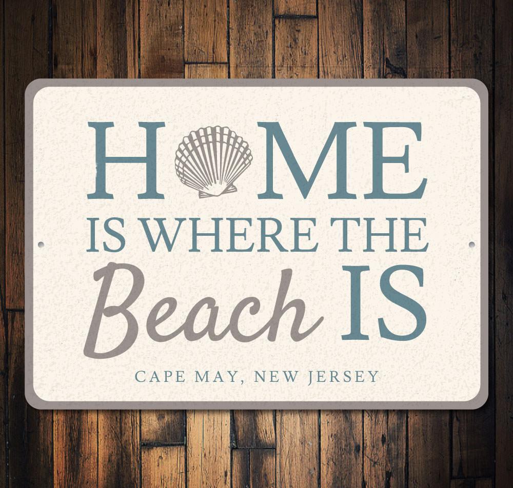 A decorative metal sign reading 'Home Is Where The Beach Is', featuring beach-themed design elements, perfect for coastal decor.