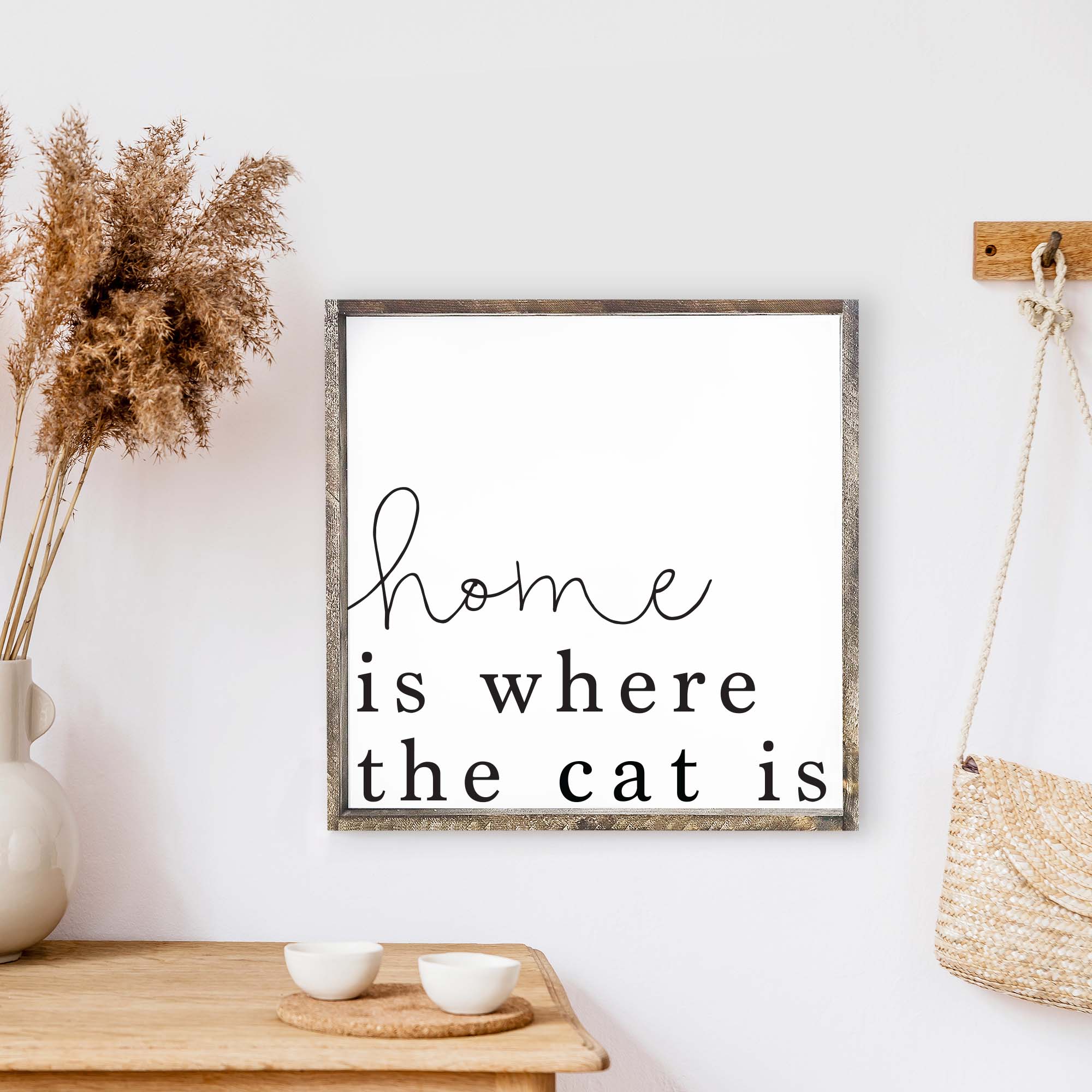 A charming wooden sign that reads 'Home Is Where The Cat Is', featuring a white background and black waterproof text, framed in stained pine wood.