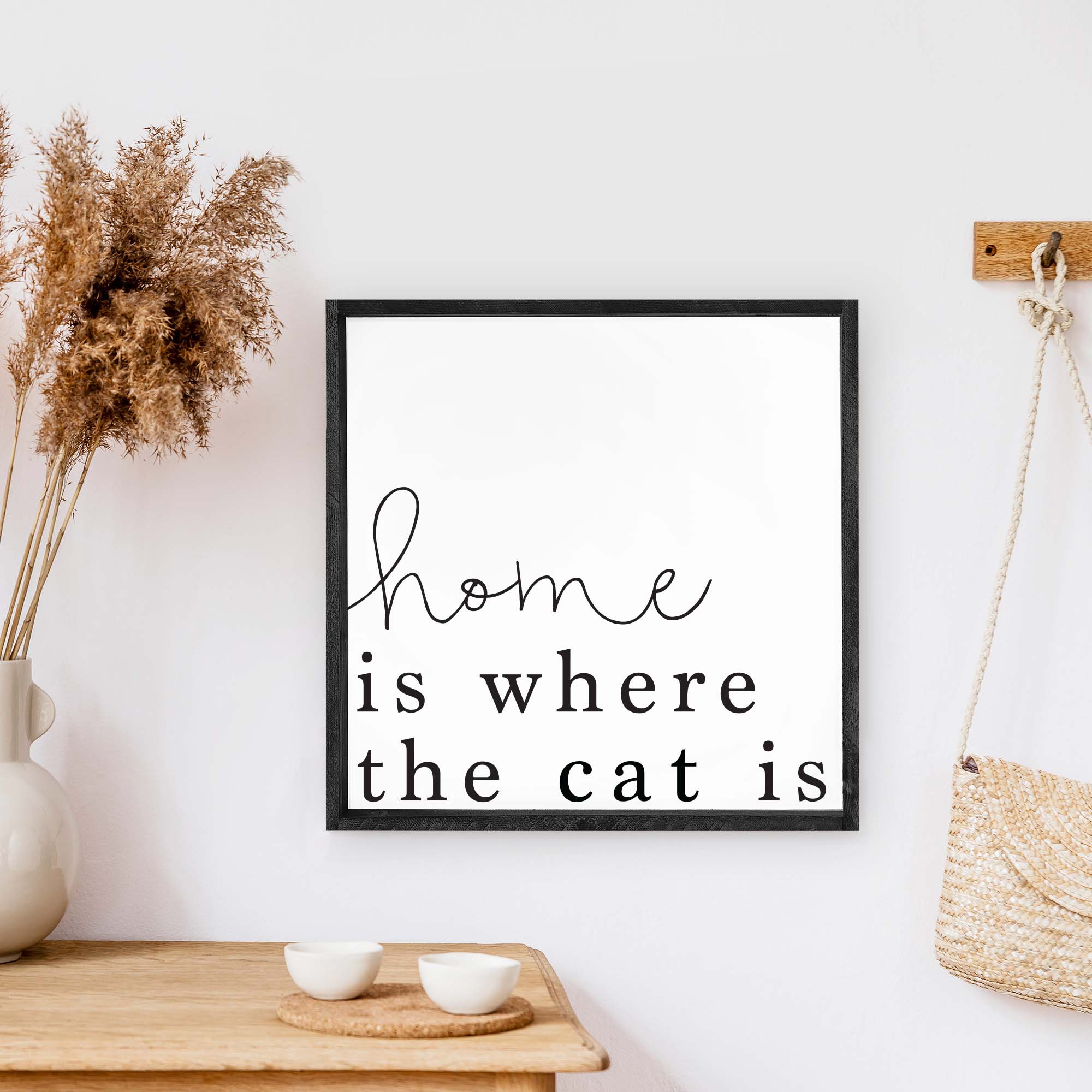 A charming wooden sign that reads 'Home Is Where The Cat Is', featuring a white background and black waterproof text, framed in stained pine wood.
