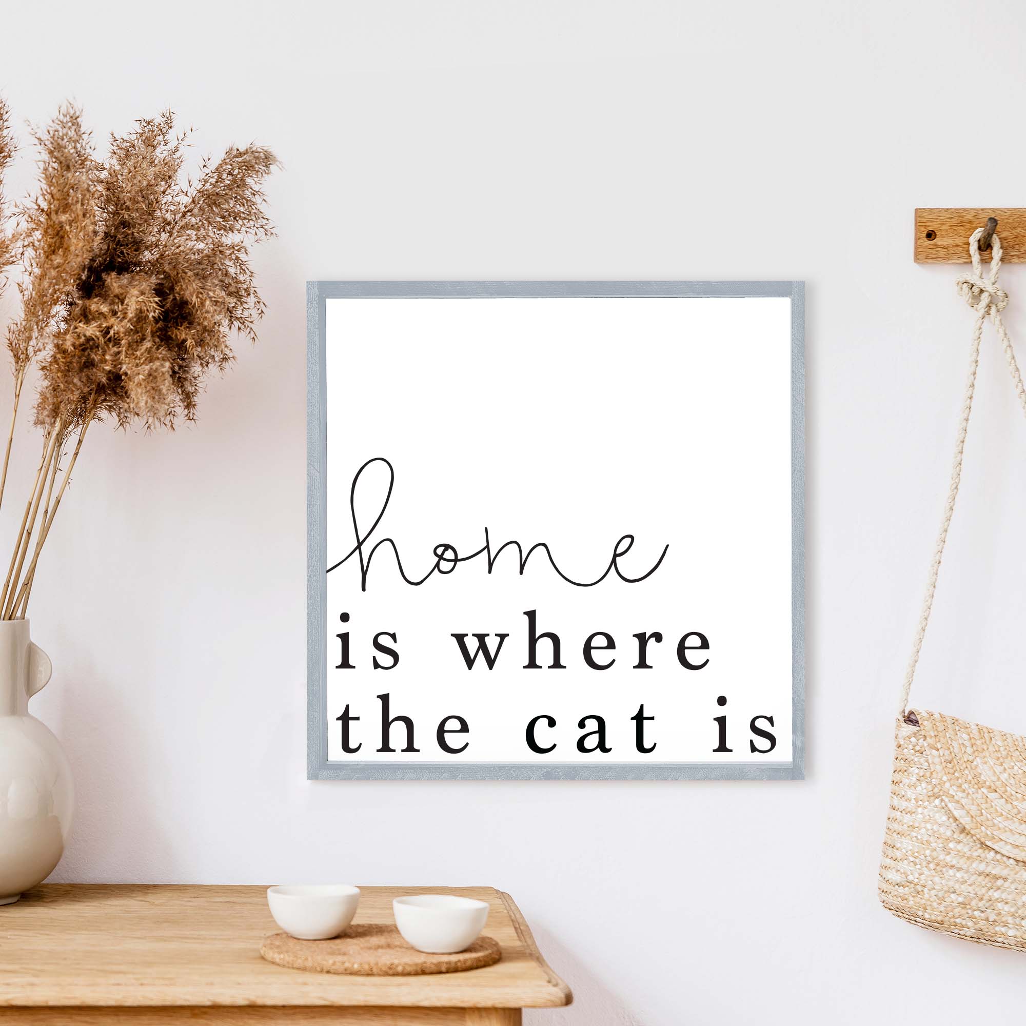 A charming wooden sign that reads 'Home Is Where The Cat Is', featuring a white background and black waterproof text, framed in stained pine wood.
