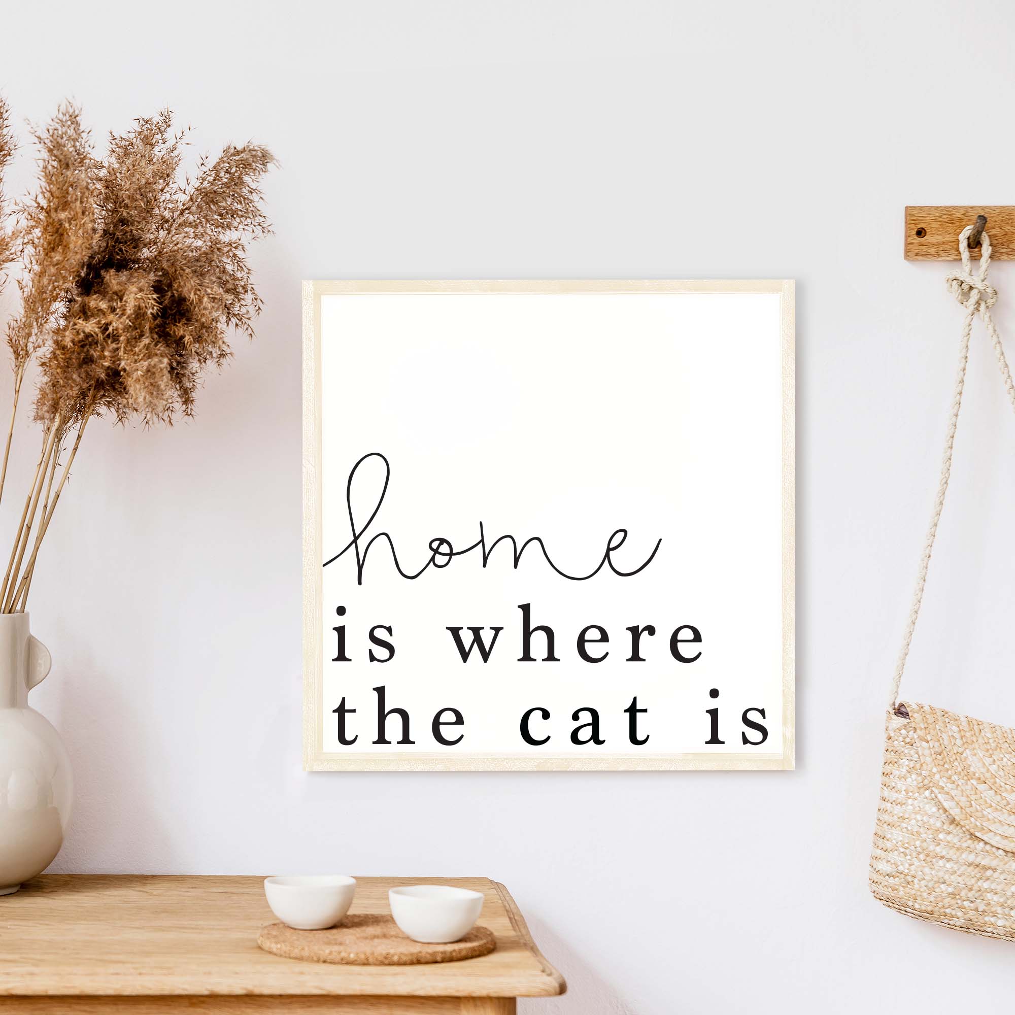 A charming wooden sign that reads 'Home Is Where The Cat Is', featuring a white background and black waterproof text, framed in stained pine wood.
