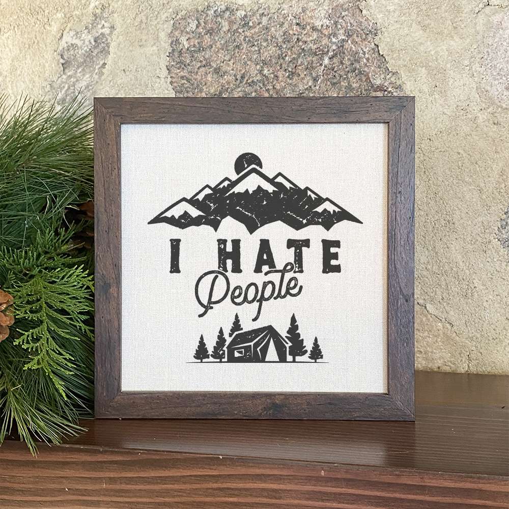 Framed sign with the text 'I Hate People' in a stylish wood frame, featuring a linen-look background.