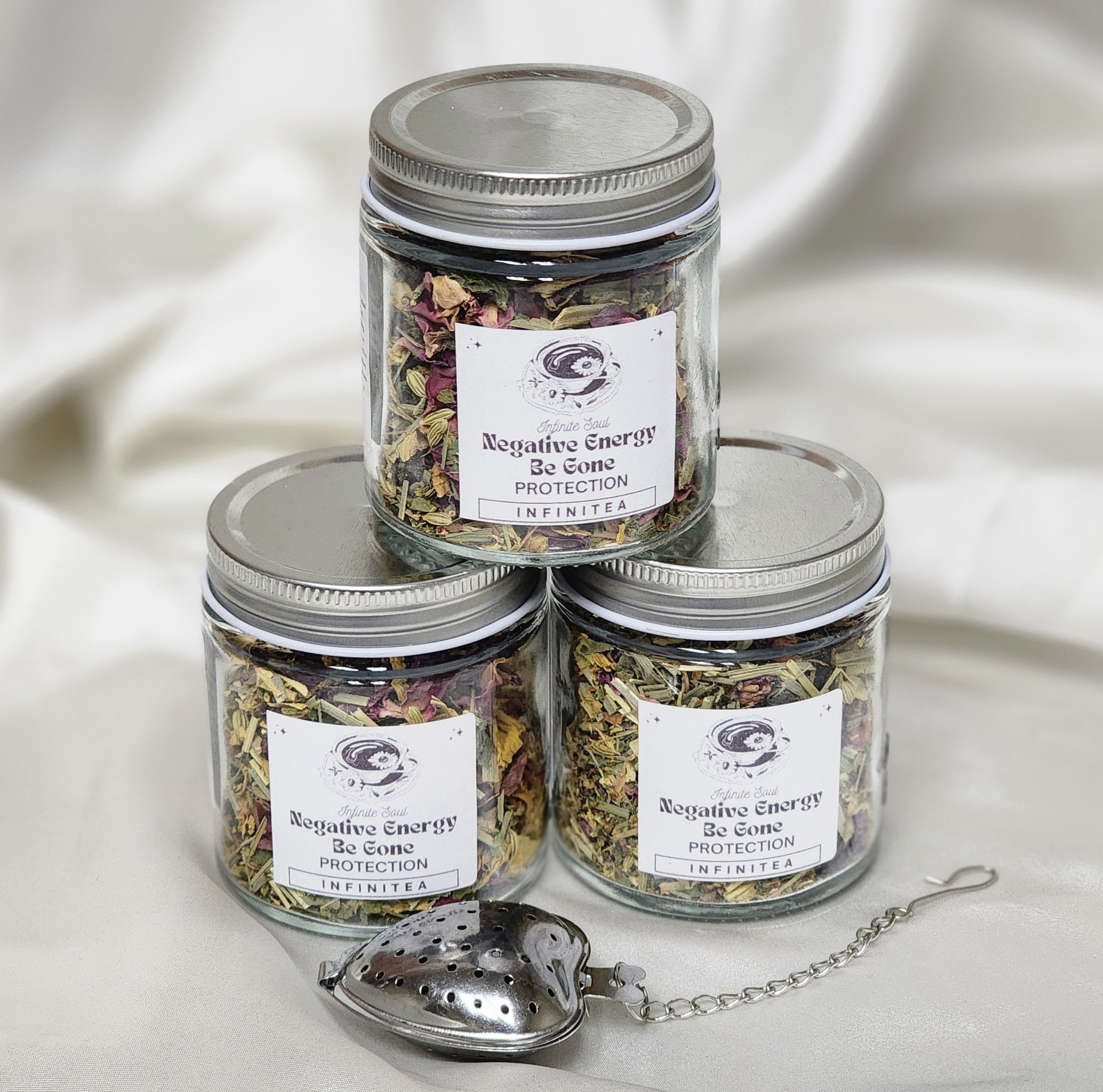 A beautifully packaged box of Infinitea Negative Energy Be Gone herbal tea blend, featuring vibrant herbs and flowers.