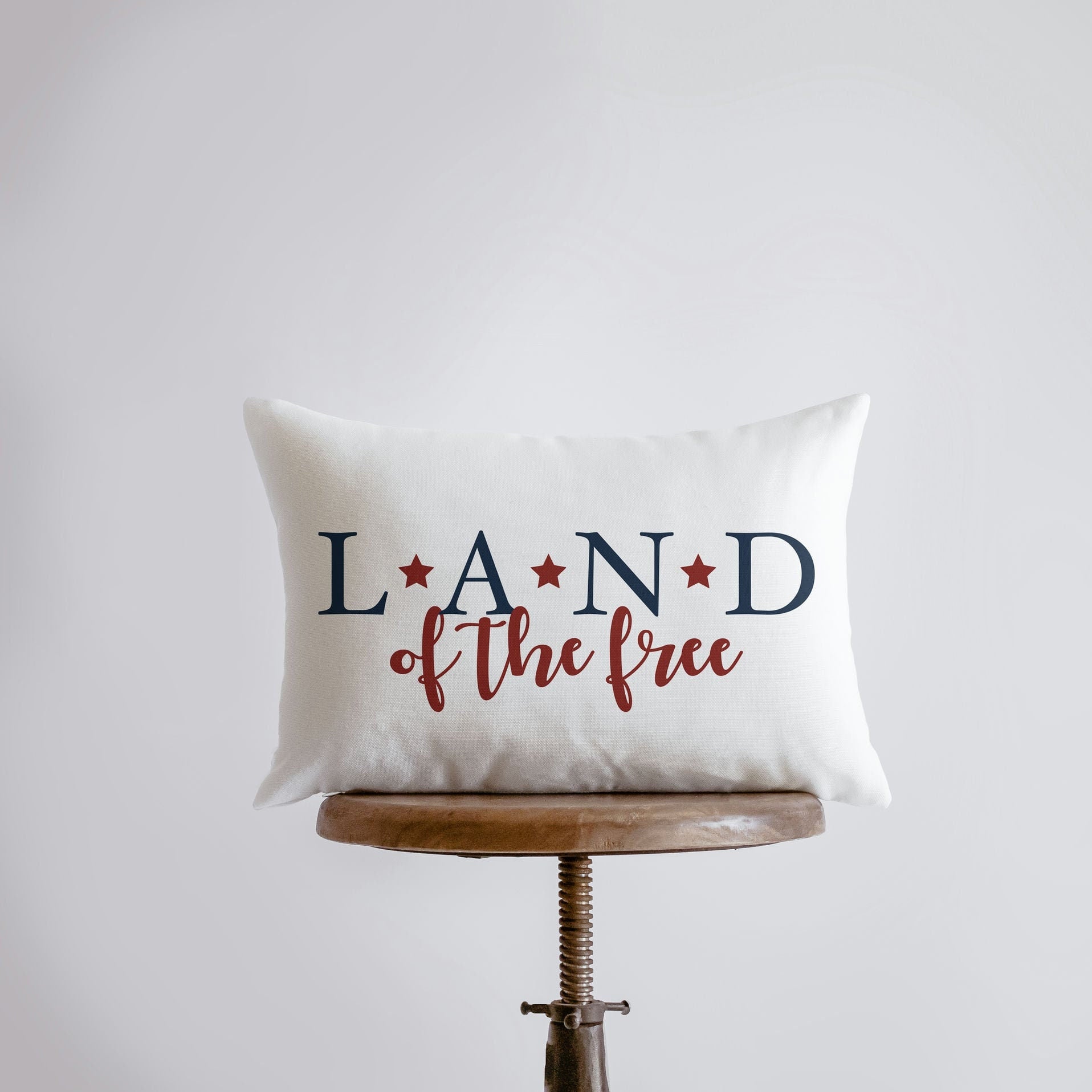 Hand-made 'Land of the Free' pillow cover featuring patriotic lettering on a brown background, perfect for Fourth of July and Memorial Day decor.