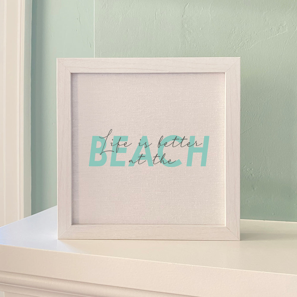 Framed sign with the text 'Life is Better at the Beach' in a stylish wood frame, showcasing a linen-look background.